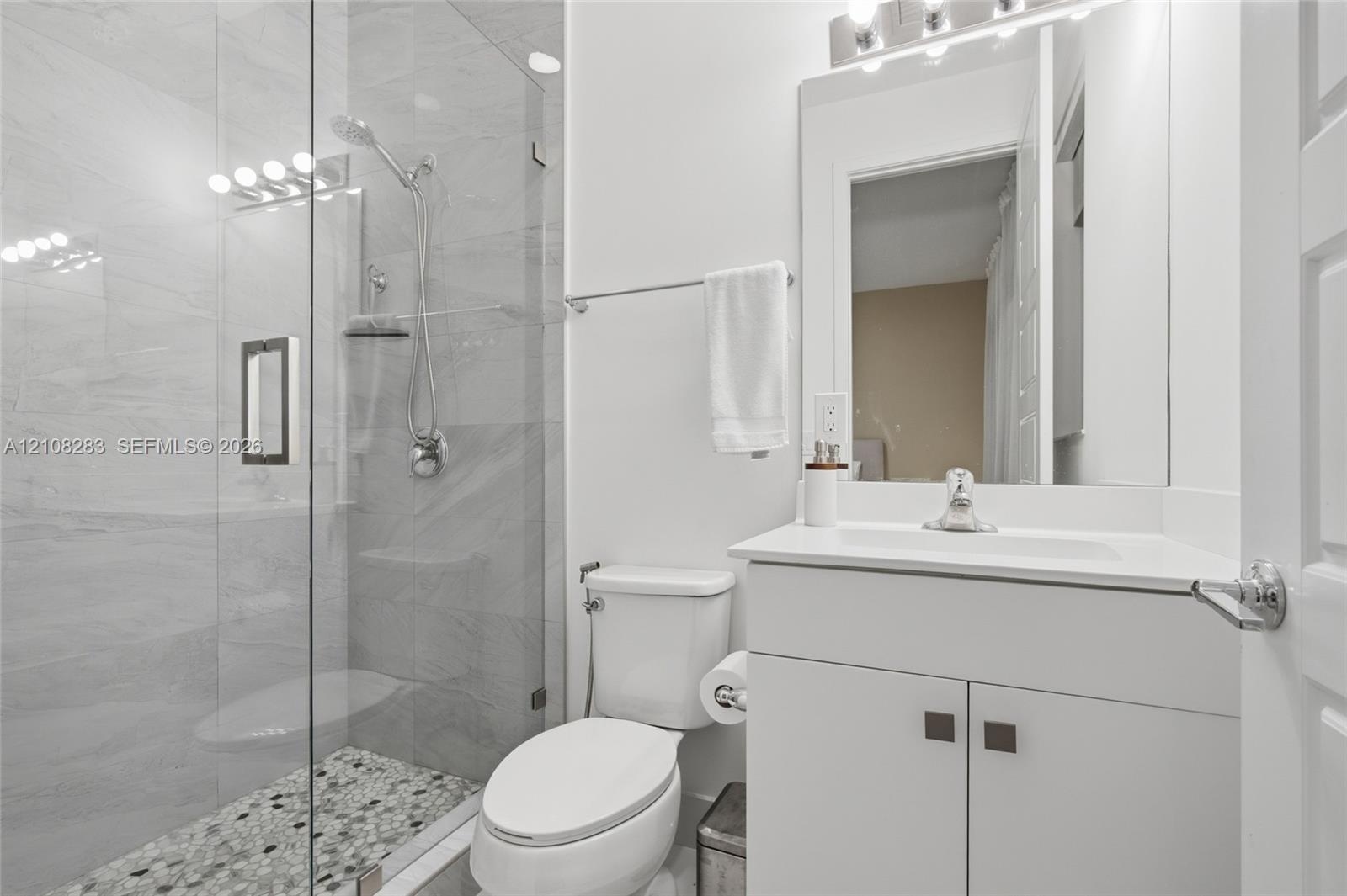 Glass-enclosed shower with stone-tile flooring, wall-mounted handheld shower head, vanity with integrated basin, and modern light fixture