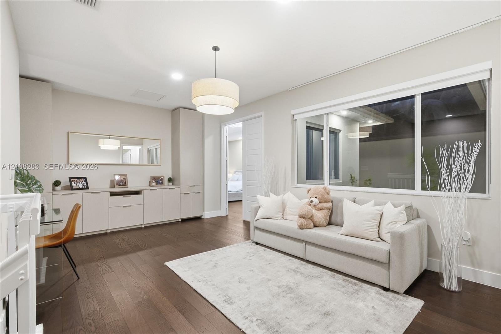 Spacious room featuring wood-finish flooring, extensive built-in cabinetry, a modern tiered drum pendant light, and a large horizontal window