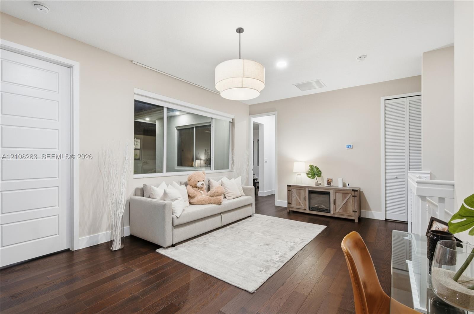 Dark wood-finish flooring, multi-panel interior door, tiered drum pendant lighting, large sliding window, and louvered closet doors