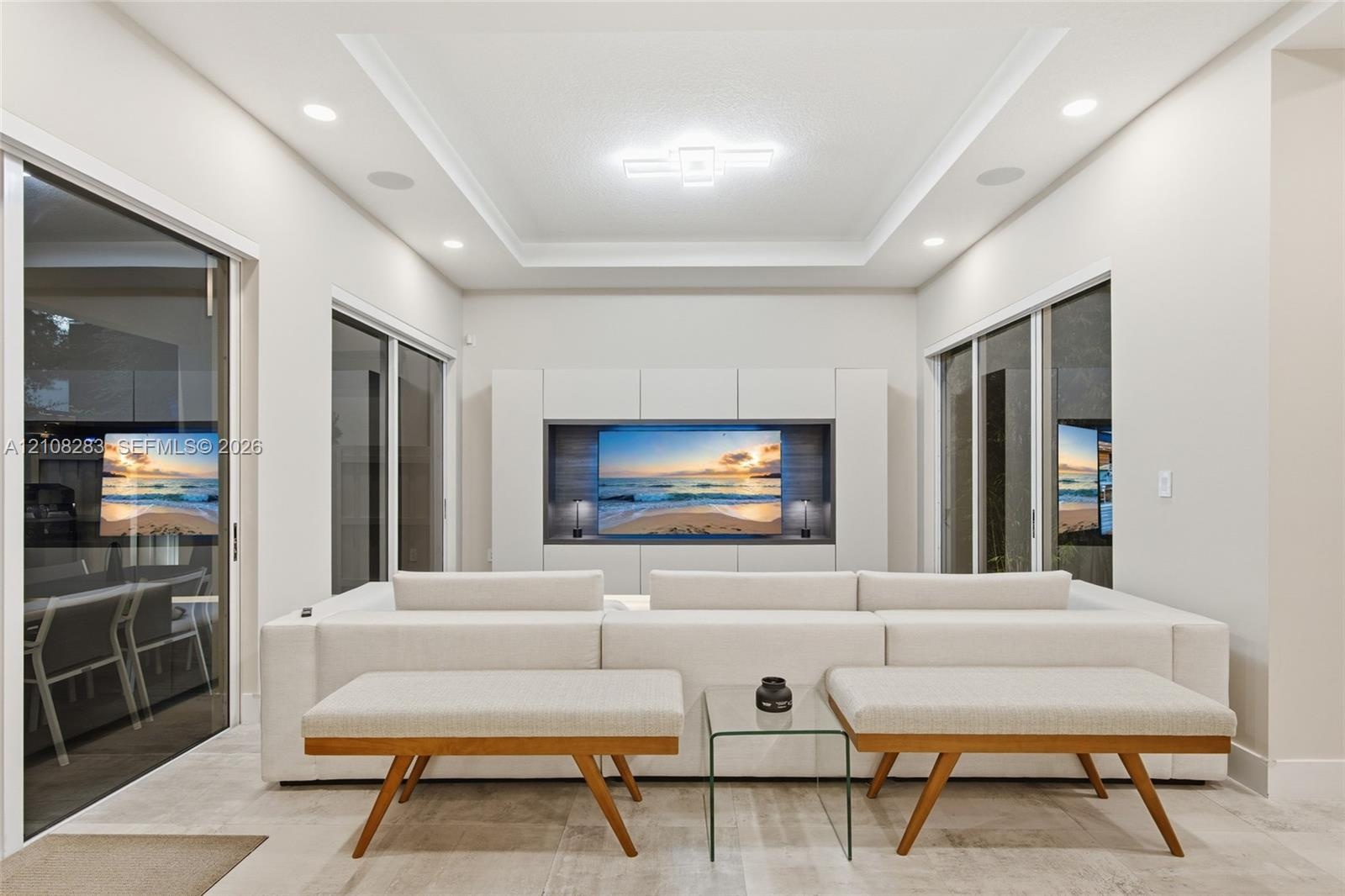 Living space featuring a tray ceiling, recessed lighting, large-format tile flooring, built-in media cabinetry, and multiple sliding glass doors