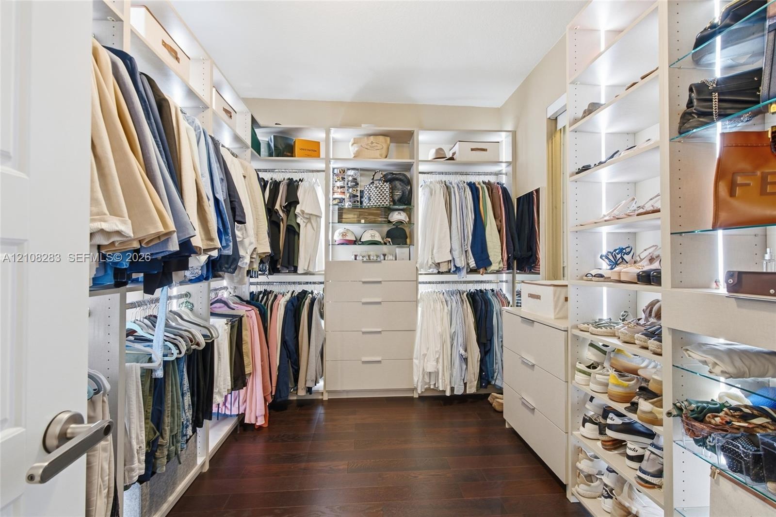 Walk-in closet featuring floor-to-ceiling custom built-in shelving, glass display shelving with integrated lighting, multi-tiered hanging rods, and in