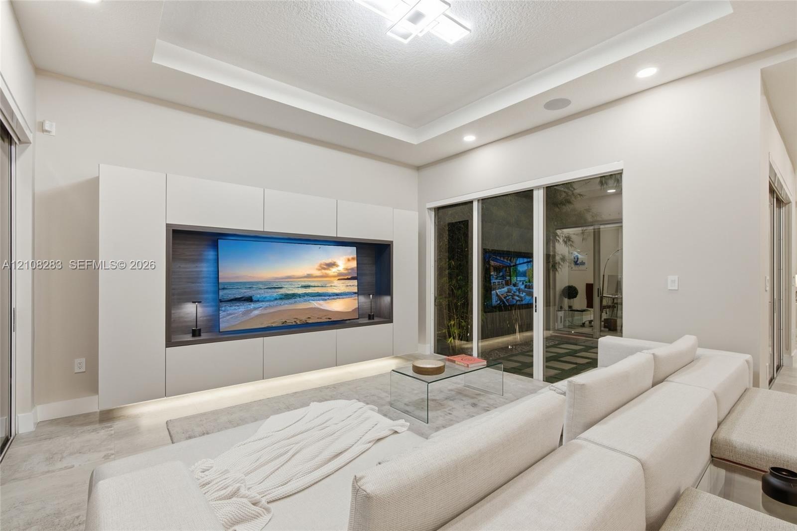Living area featuring a tray ceiling with recessed lighting, custom floor-to-ceiling built-in media cabinetry with integrated lower illumination, and 