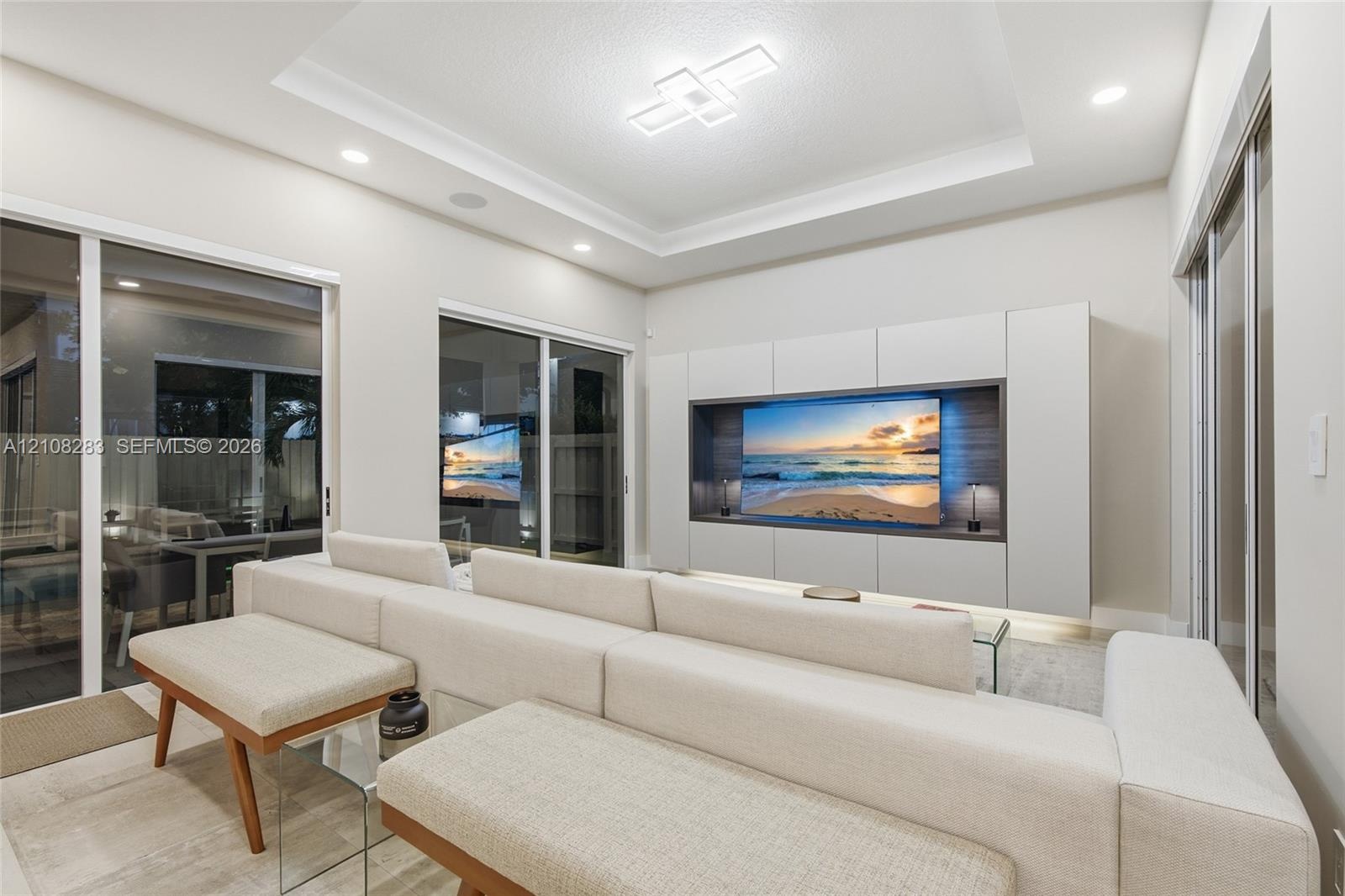 Tray ceiling with integrated geometric lighting, large-format tile flooring, and custom built-in cabinetry featuring recessed media display with wood-