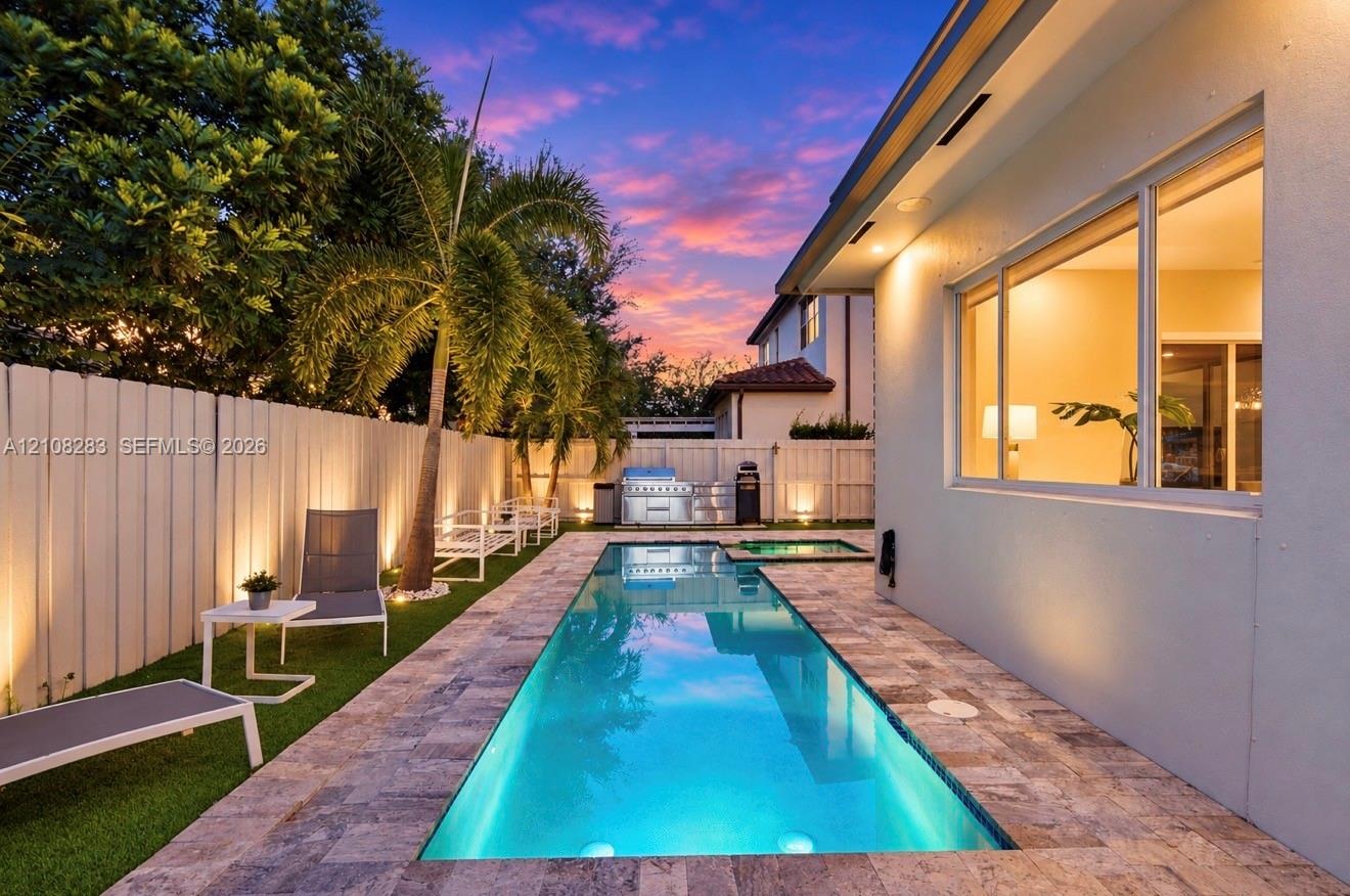 Rectangular swimming pool featuring a stone-paver surround, integrated spa, built-in outdoor grill station, and artificial turf lawn, enclosed by priv