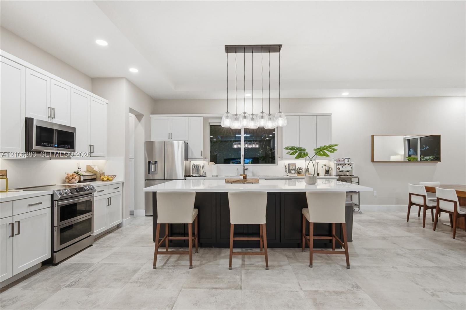 Kitchen featuring white shaker-style cabinetry, a contrasting dark-toned kitchen island with a light-toned solid surface countertop, stainless steel a