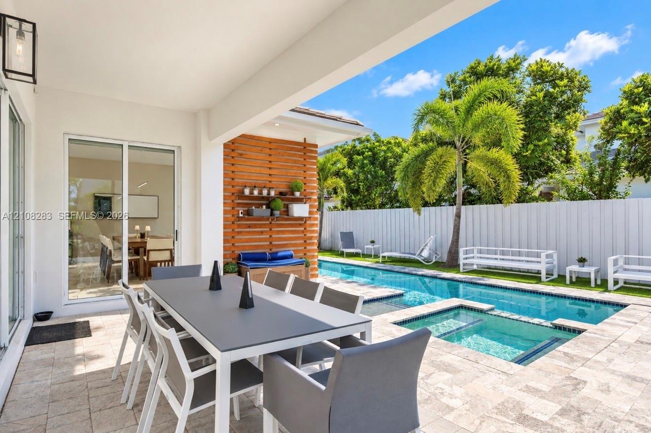 Covered patio featuring stone paver flooring, horizontal slat wood accent wall, built-in shelving, swimming pool with integrated spa, and vertical pri