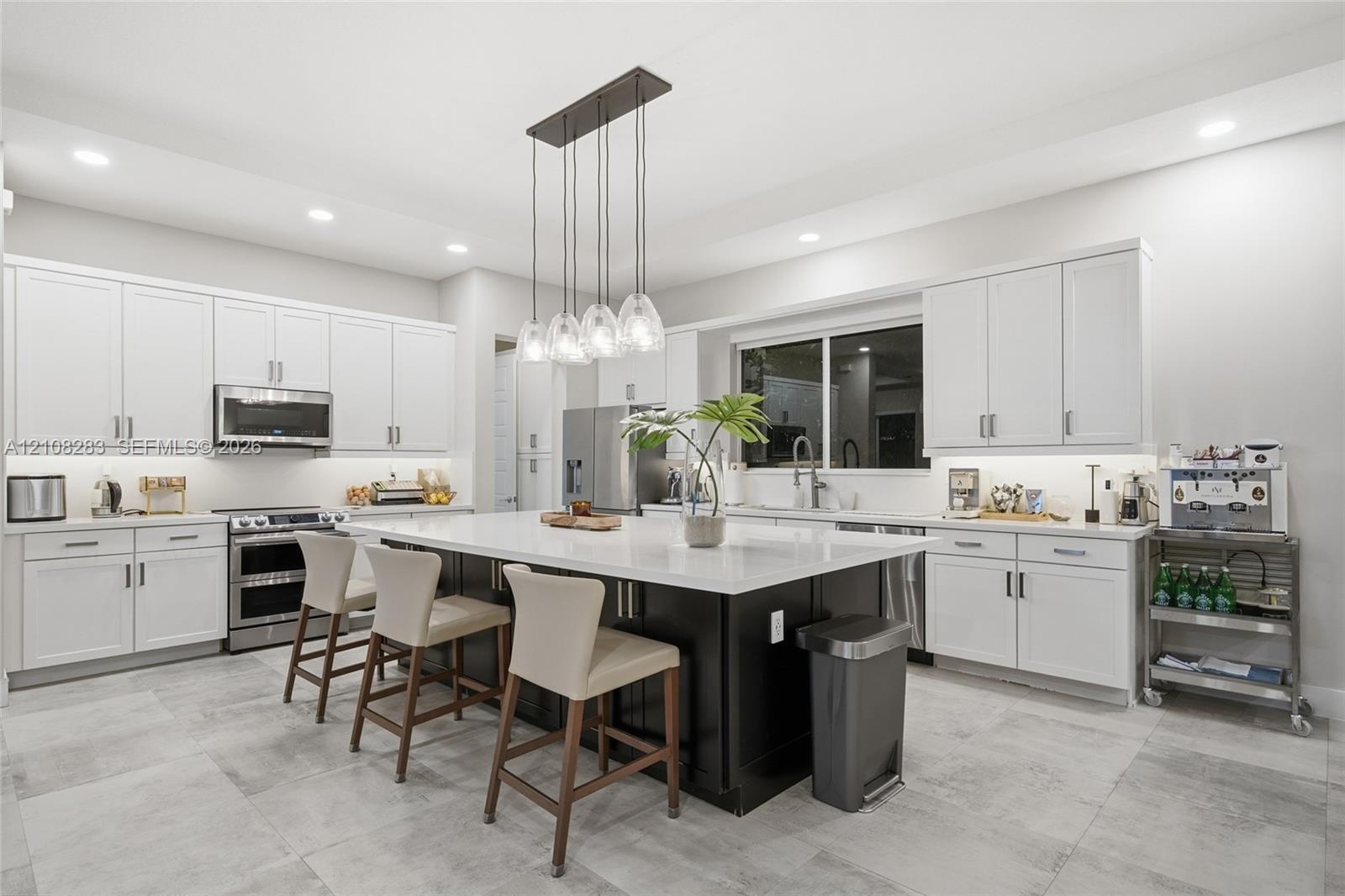 Kitchen featuring white Shaker-style cabinetry, a central island with a contrasting dark base and stone countertop, stainless steel appliances, recess
