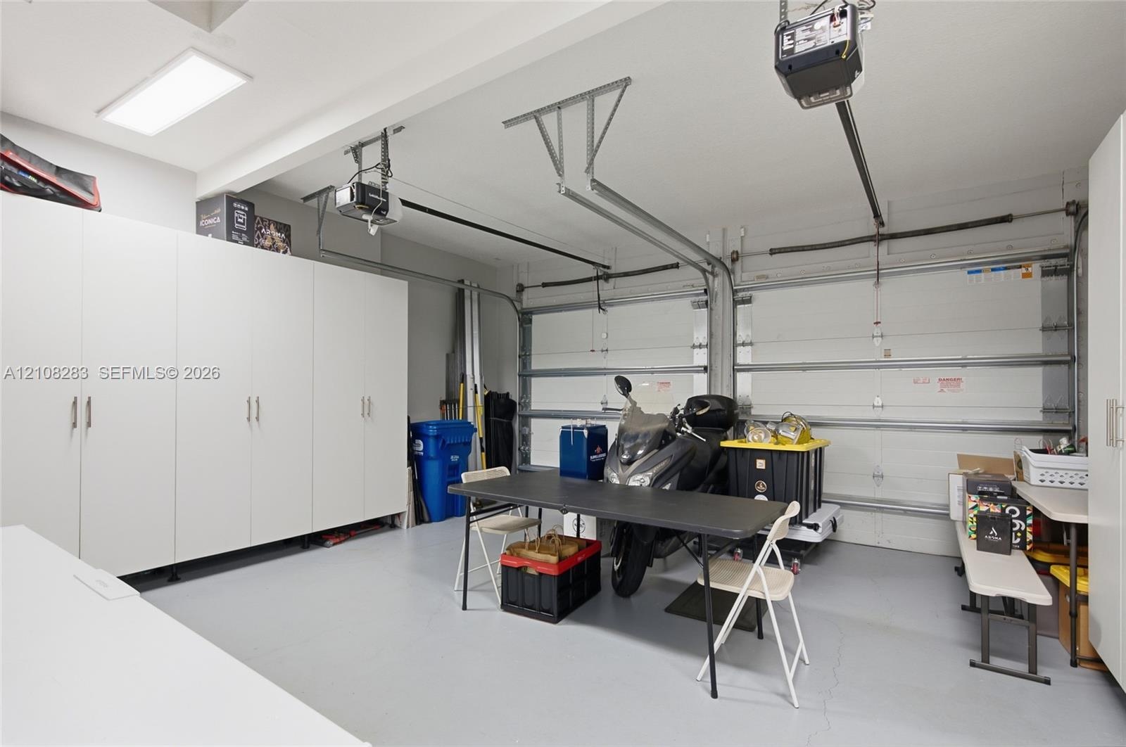 Two-car garage featuring a sealed concrete floor, dual automatic garage door openers, and extensive floor-to-ceiling built-in white cabinetry