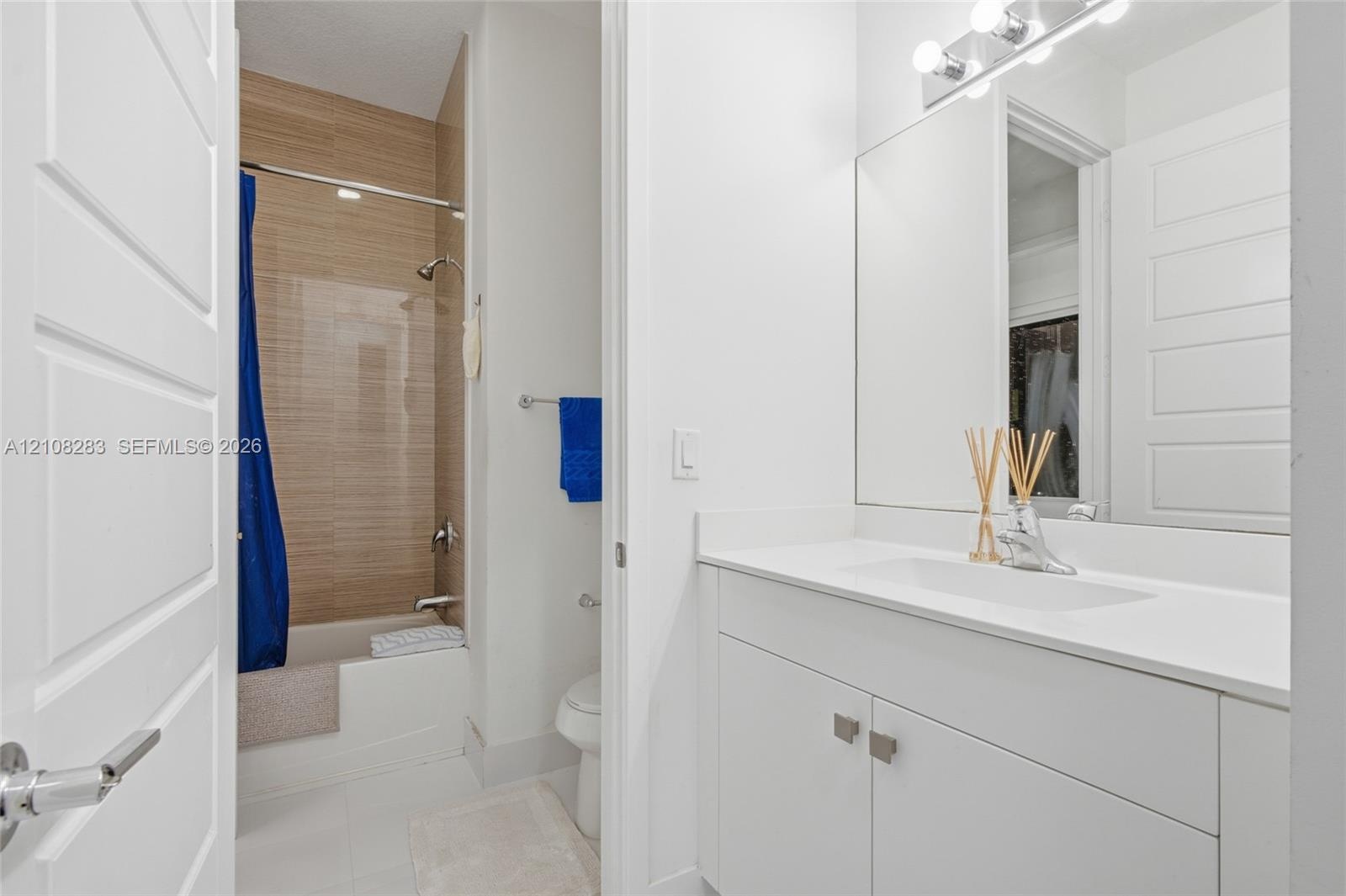 Bathroom featuring a white vanity with a composite countertop, an integrated rectangular sink, a floor-to-ceiling tiled shower surround with a light w