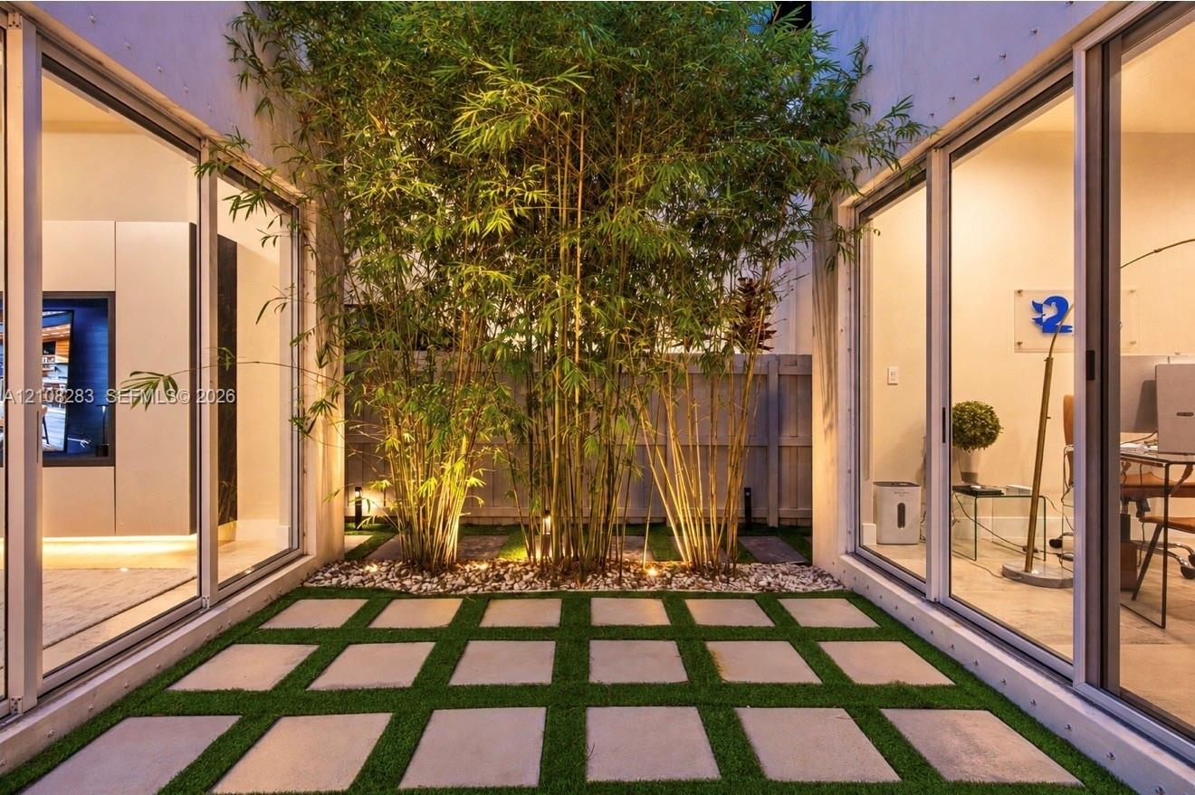 Central atrium featuring large-format concrete pavers, integrated synthetic turf grid, mature bamboo specimens, and expansive floor-to-ceiling sliding