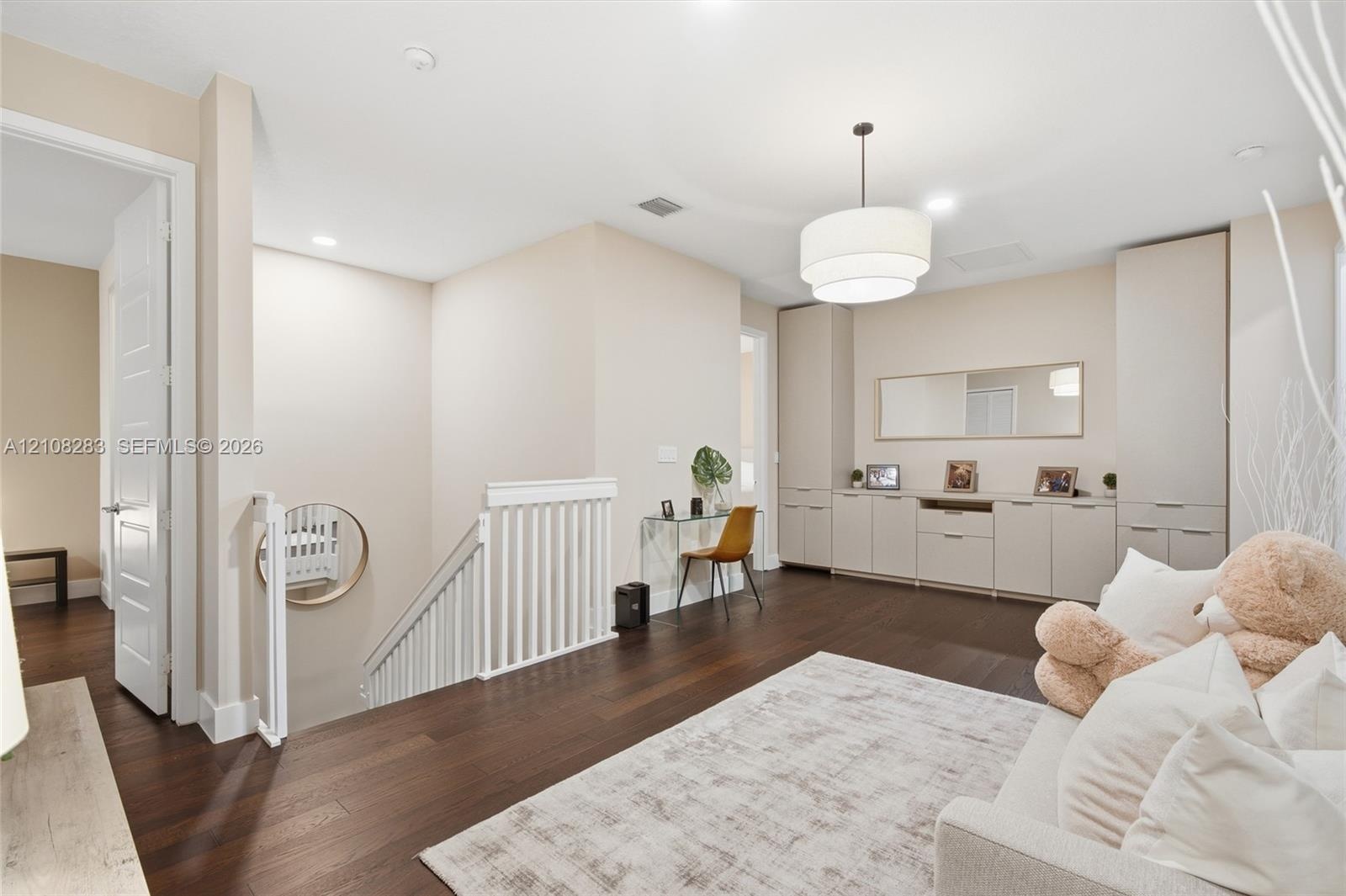 Dark wood-finish flooring, built-in floor-to-ceiling cabinetry with integrated storage, white spindle staircase railing, and a tiered drum pendant lig