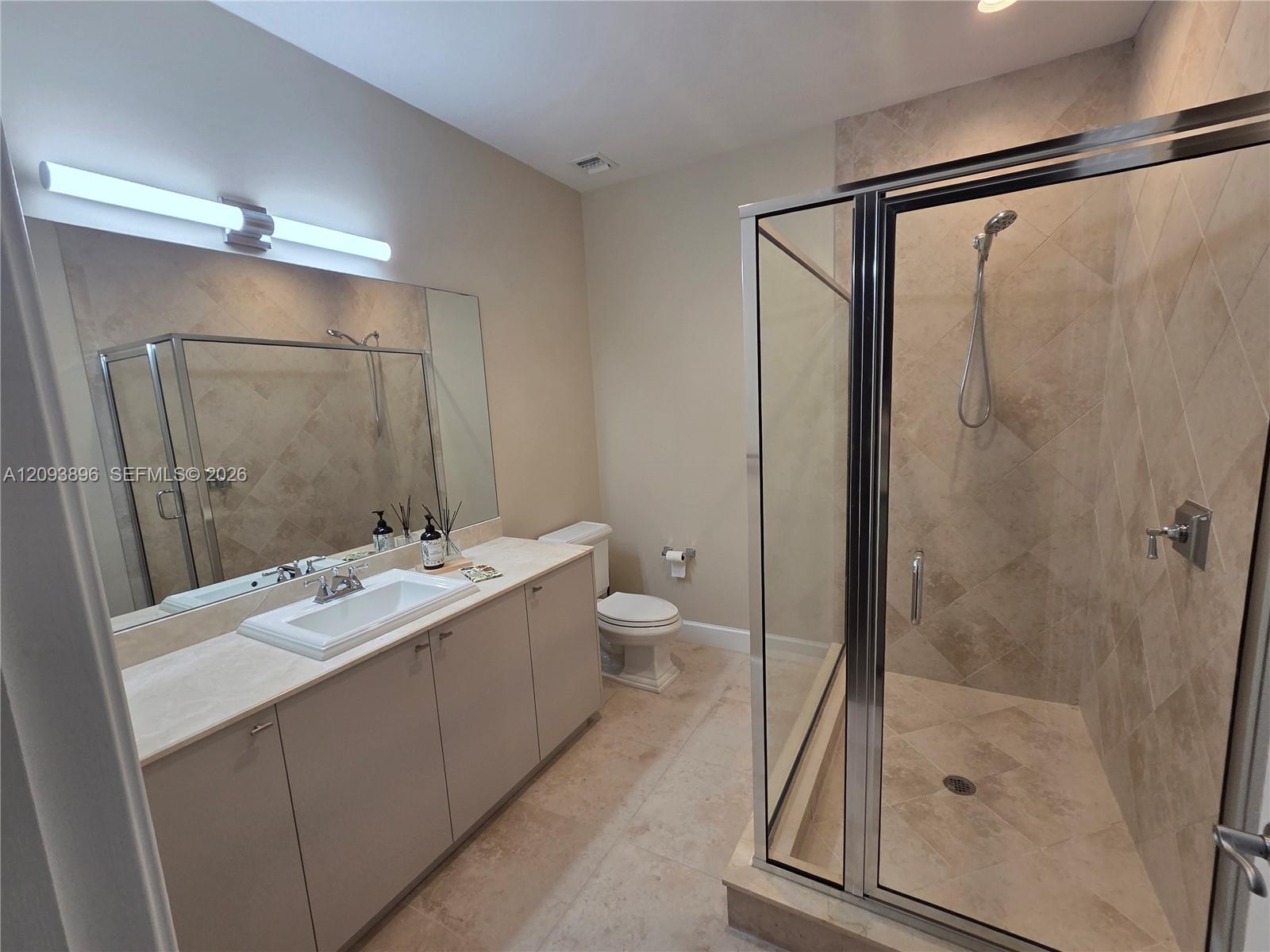 Bathroom featuring a long vanity with stone-style countertop and integrated sink, full-width mirror, glass-enclosed shower with tiled surround, and ce