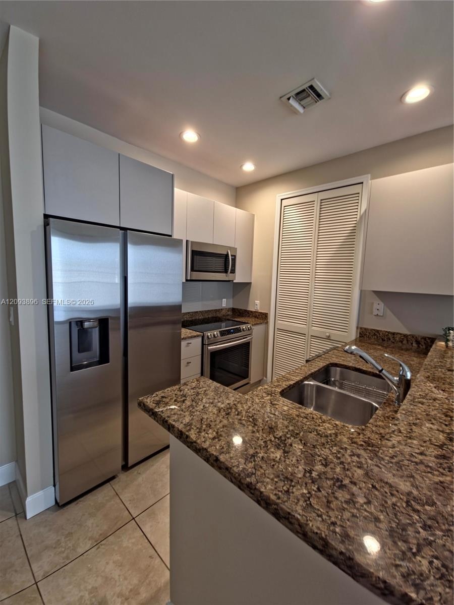 Kitchen featuring flat-panel cabinetry, stone countertops, stainless steel appliances, double-basin sink with a gooseneck faucet, and tile flooring