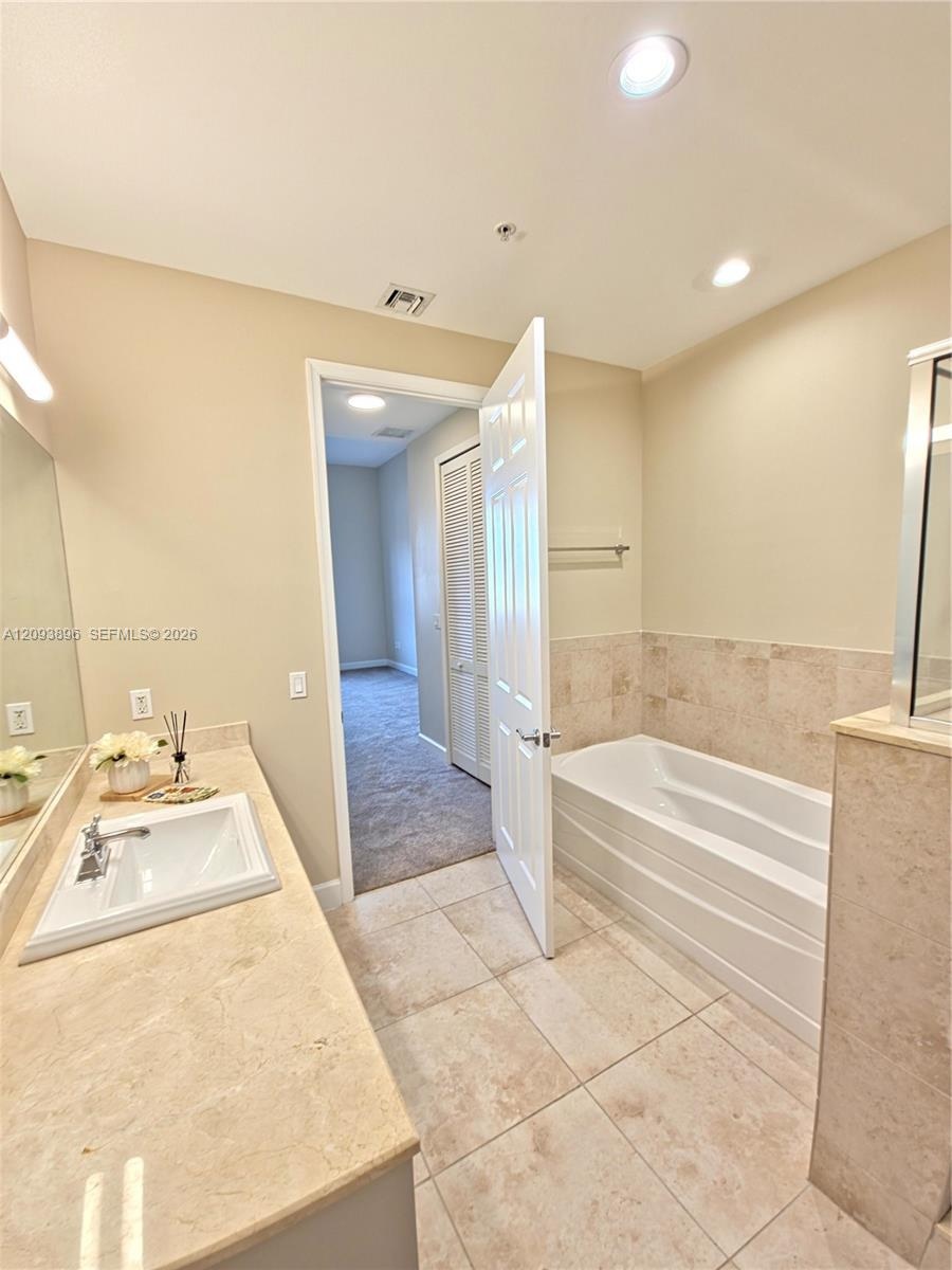 Bathroom featuring a rectangular undermount sink, stone-finish countertop, tile flooring, and a tiled soaking tub surround