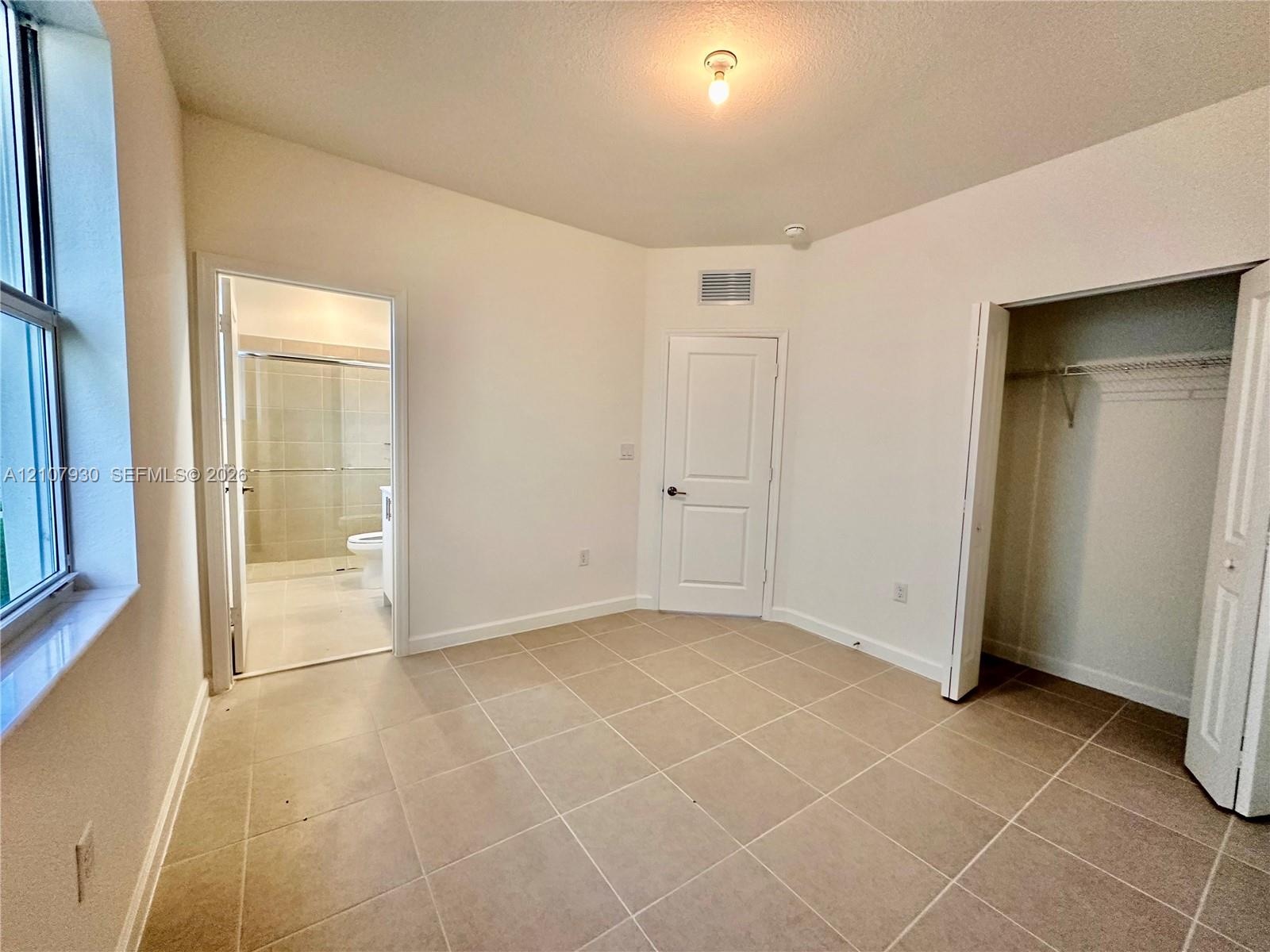 Room featuring tile flooring, neutral wall color, multi-panel interior door, walk-in closet with built-in shelving, and flush-mount ceiling light