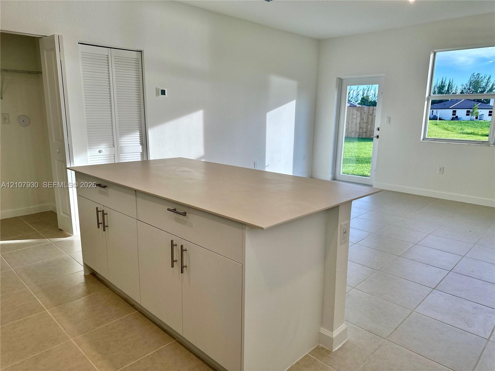 Center island featuring white cabinetry with metallic pulls and a neutral-toned countertop, set against tile flooring throughout the interior