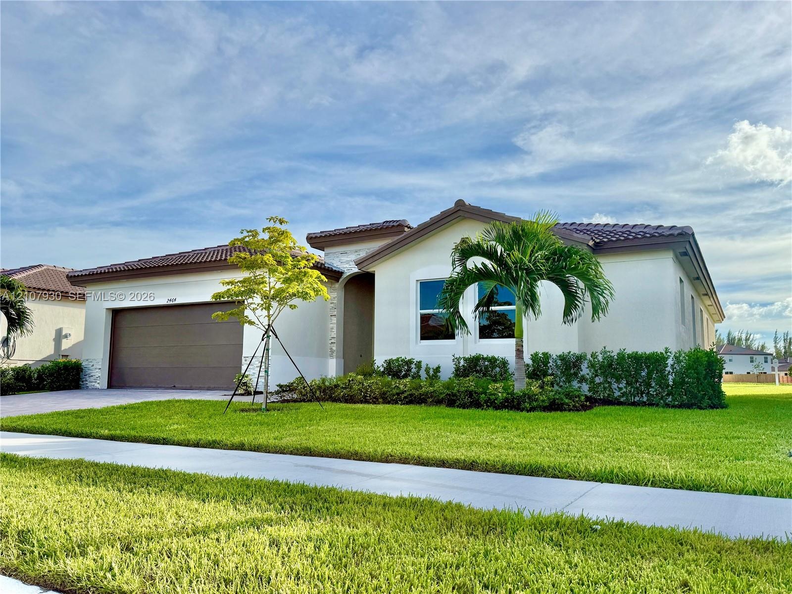 Single-story exterior featuring a tile roof, light-toned stucco facade, stone masonry accents, multi-car garage, and manicured landscaping