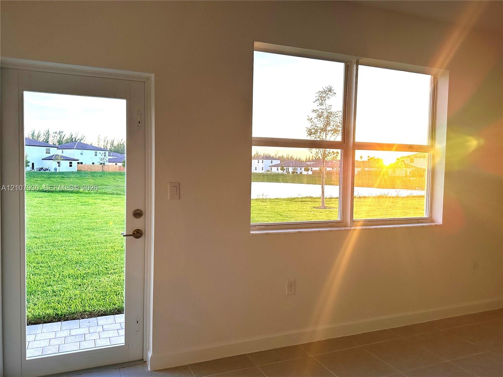 Full-length glass-panel door, large dual-pane windows, neutral tile flooring, and exterior water backdrop