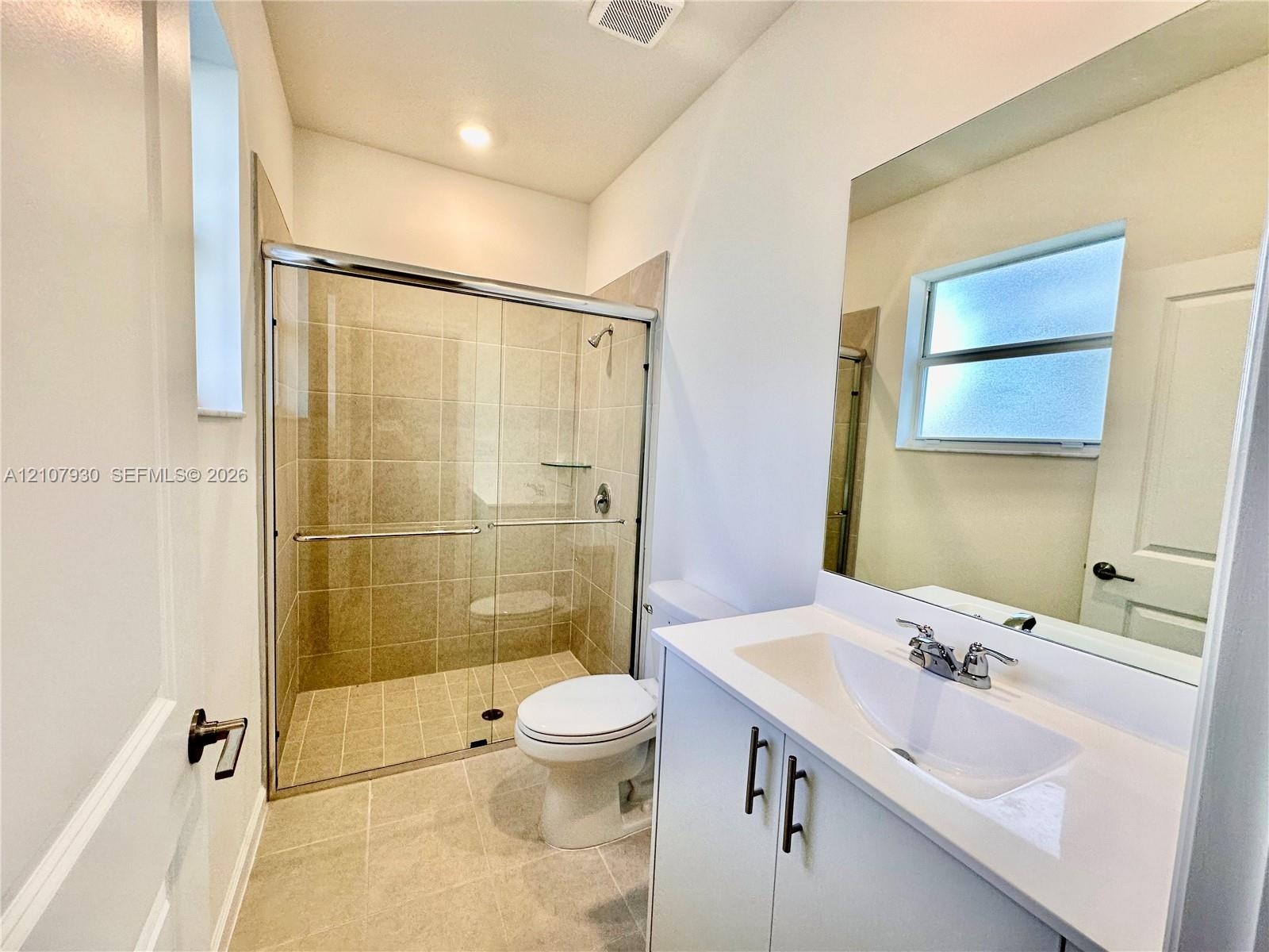 Bathroom featuring a glass-enclosed shower with tile surround, white vanity cabinet with a stone-composite countertop, undermount sink, and large wall