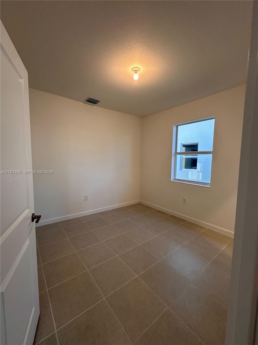 Neutral-toned interior room featuring large-format ceramic tile flooring, a single-hung window, and a crisp white six-panel door