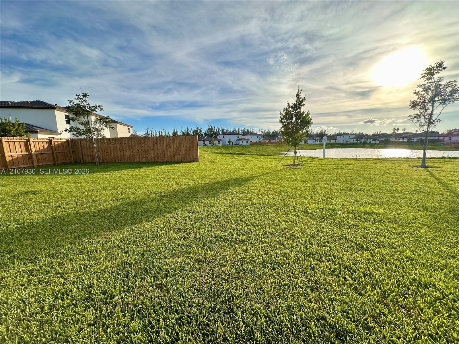 Expansive backyard featuring a large grass lawn, perimeter wood fencing, and waterfront property boundaries