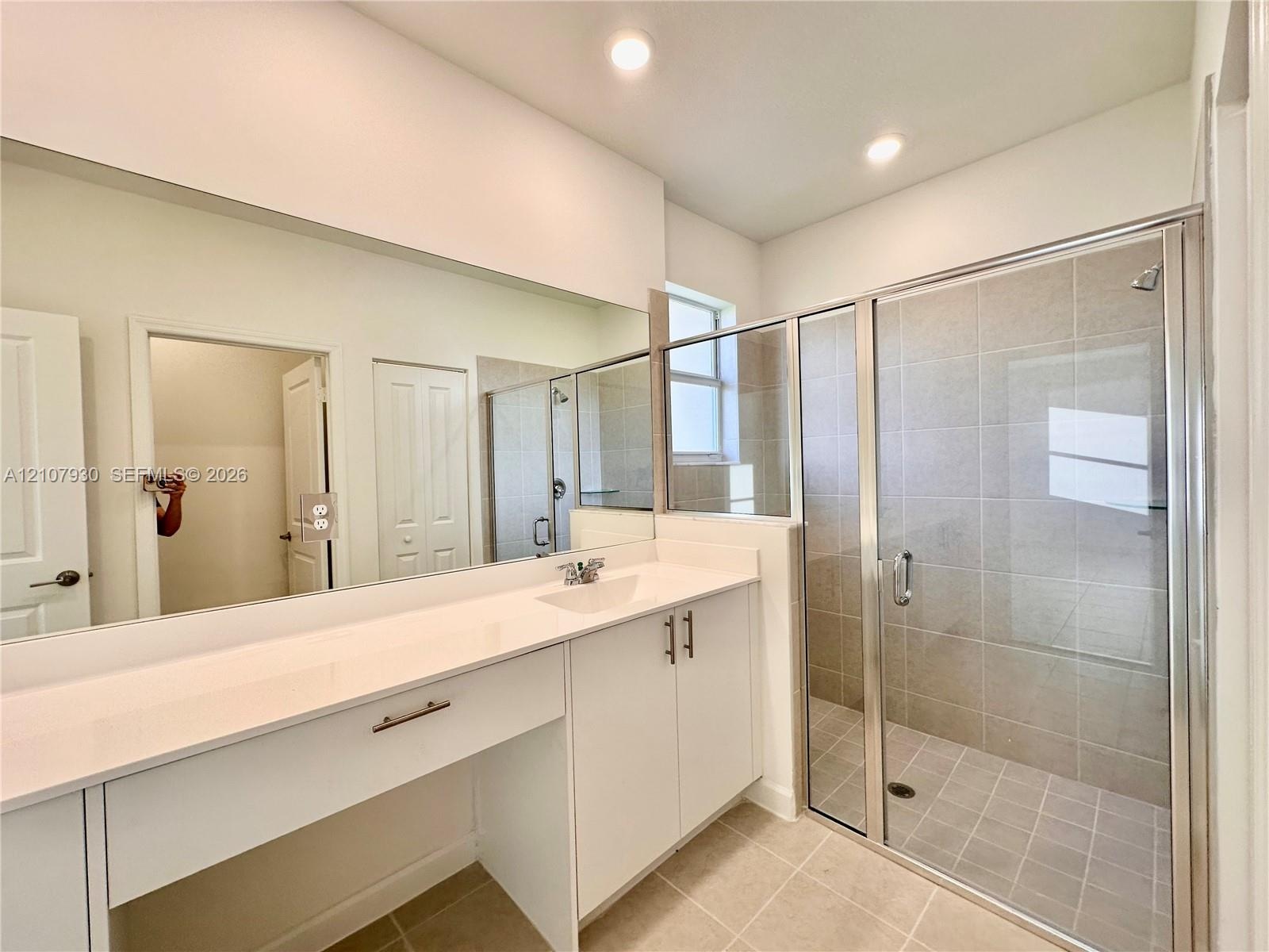 Bathroom featuring a white vanity with a solid-surface countertop, an integrated sink, full-width vanity mirror, walk-in shower with tile surround, an