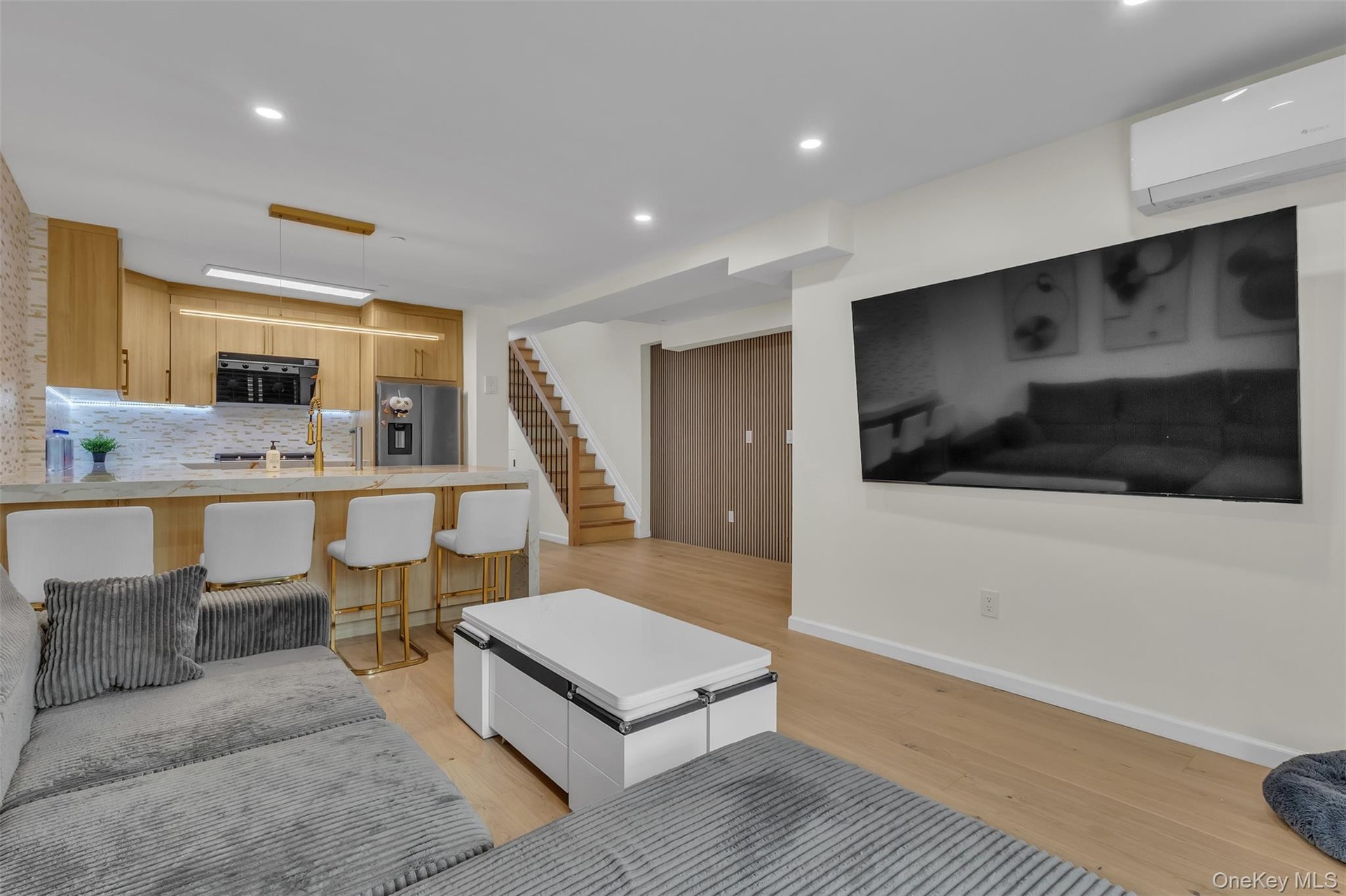 Open-concept kitchen featuring light wood-finish cabinetry, a stone-patterned island countertop, recessed lighting, wood-finish flooring, and a wall-m