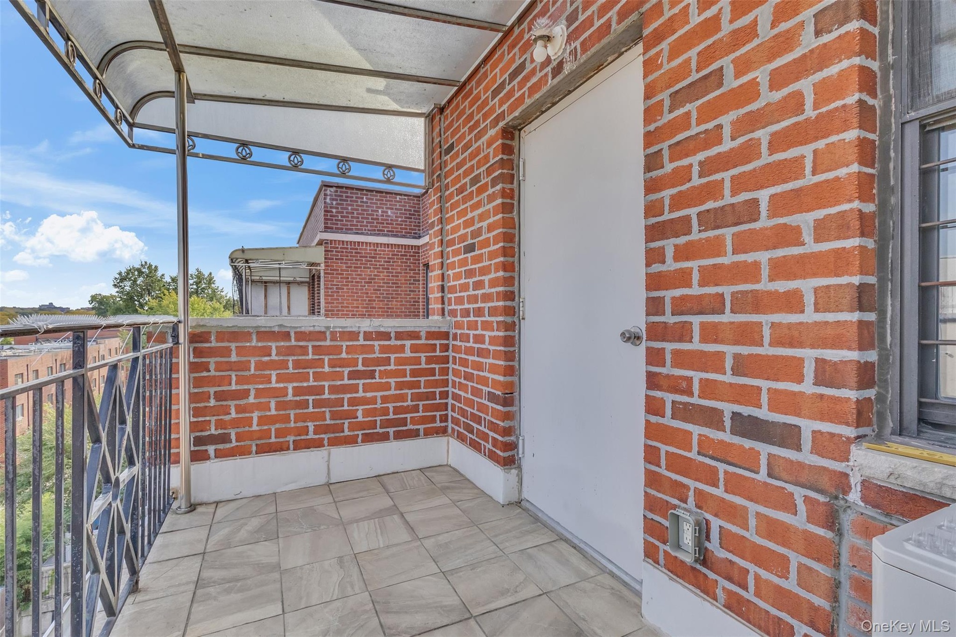 Balcony featuring red brick exterior walls, stone-finish tile flooring, metal railing, and a fixed overhead awning