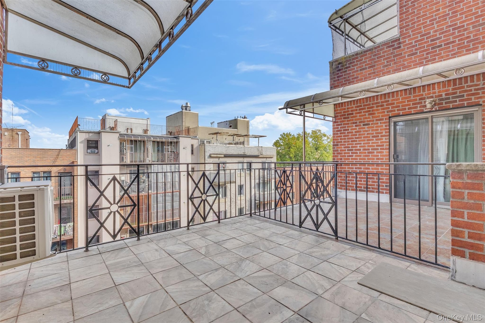 Spacious outdoor terrace featuring tiled flooring, wrought-iron railings, an overhead awning, and exterior brick masonry