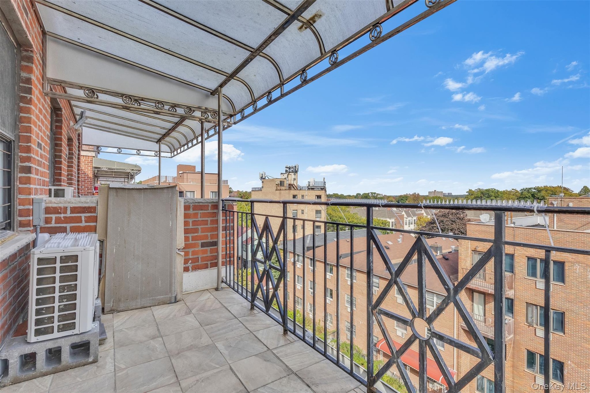 Private balcony featuring a geometric black metal railing, overhead awning, brick facade, and tile flooring