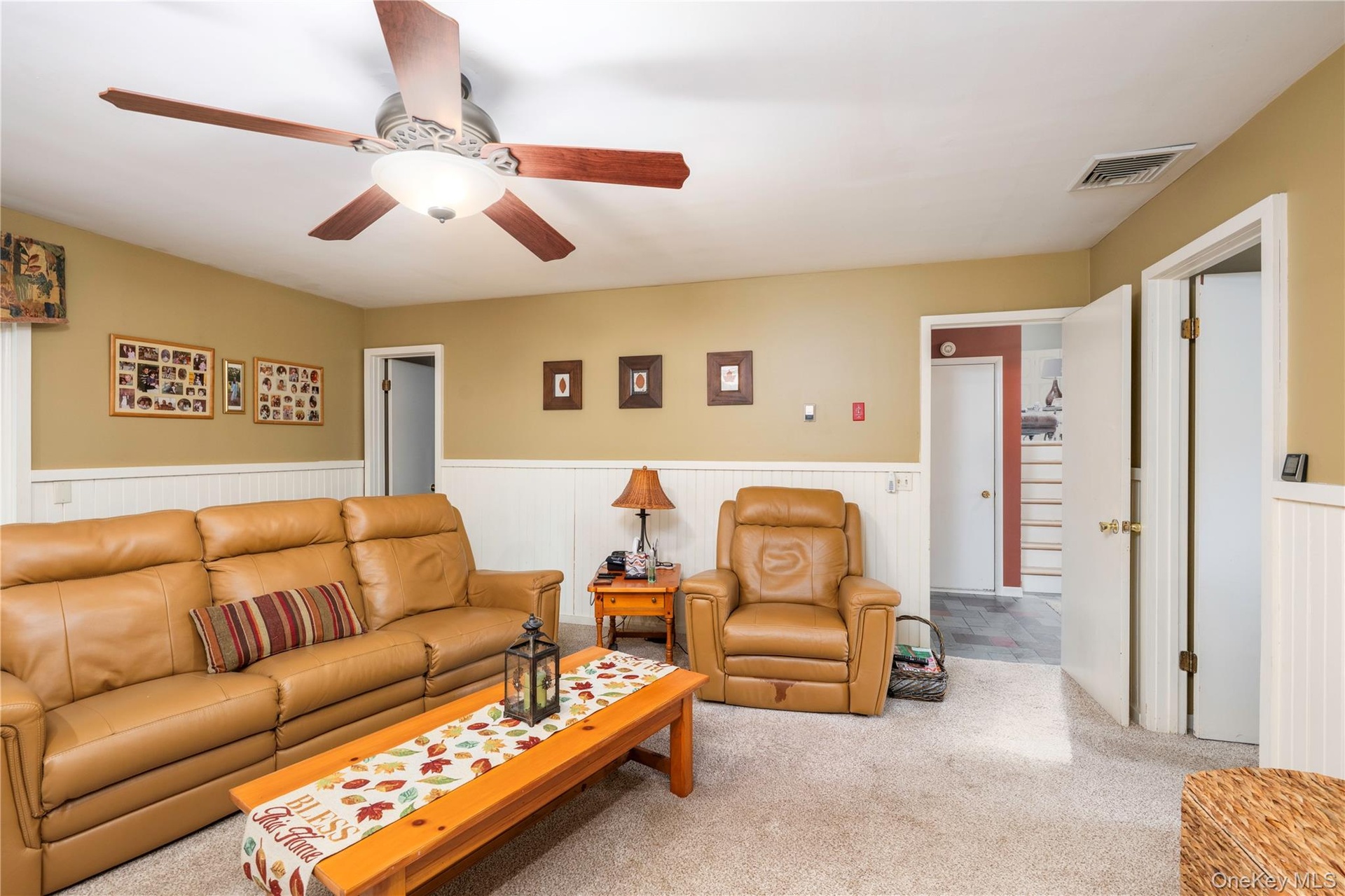 Interior space featuring wall-mounted wainscoting, carpeted flooring, and a ceiling-mounted light fixture with a fan