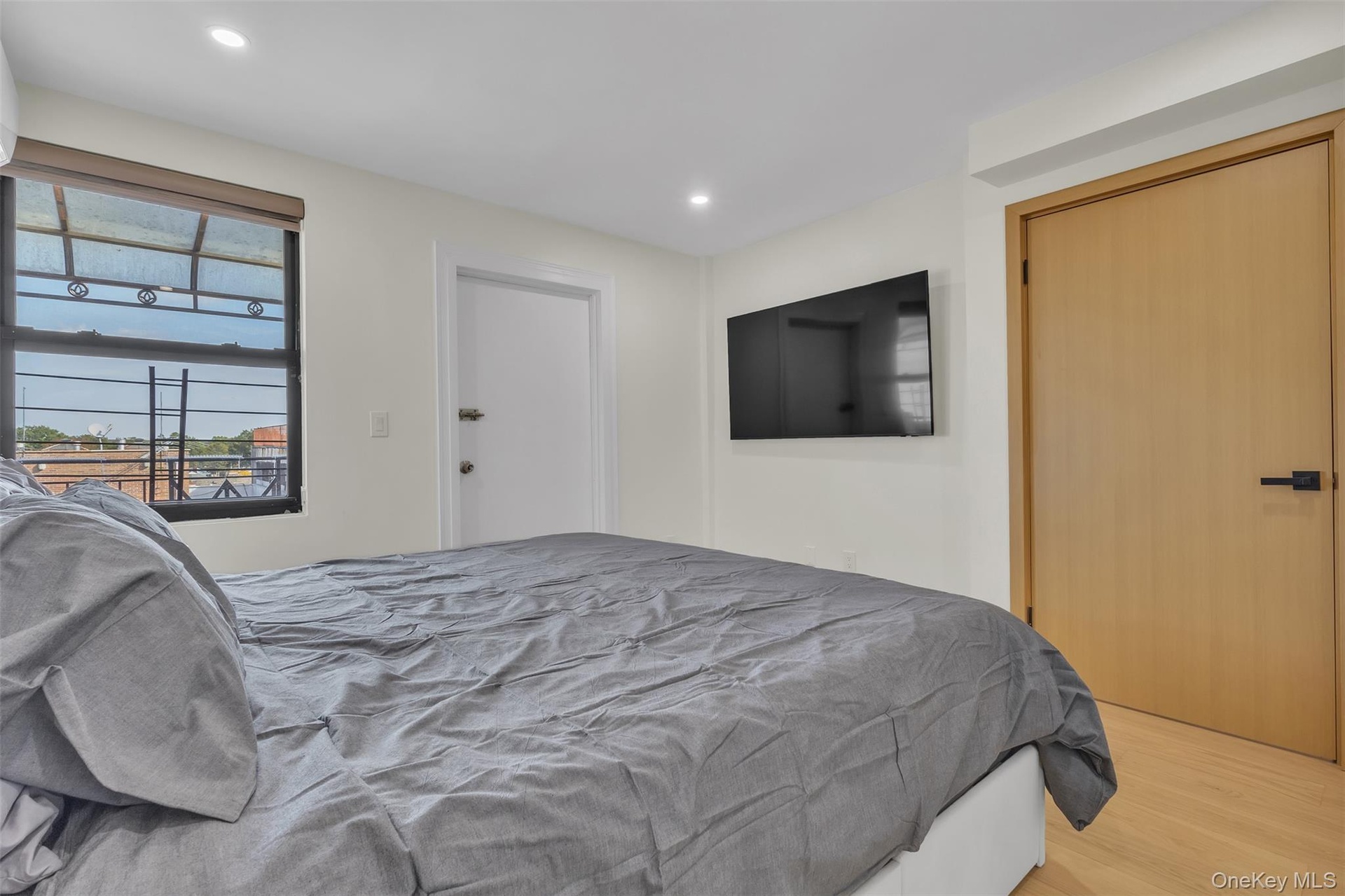 Wood-finish flooring, recessed lighting, solid-core light wood door with matte black hardware, and an expansive window with dark framing