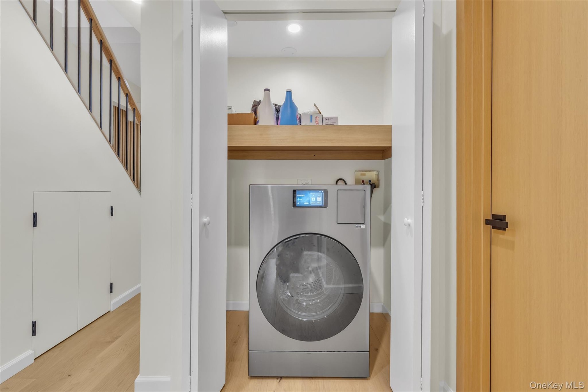 Laundry closet featuring a stainless-steel washer-dryer combination unit, custom built-in wood shelving, wood-finish flooring, and double-hinged doors