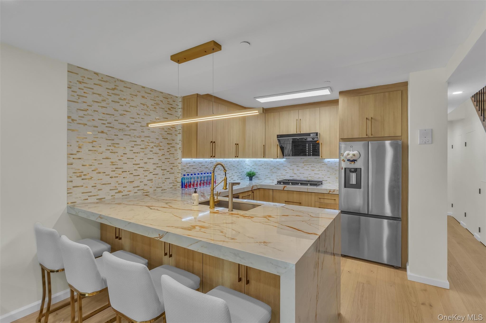 Kitchen featuring a waterfall-edge island with stone-finish countertops, wood-finish cabinetry, a tiled backsplash, wood-finish flooring, and a linear