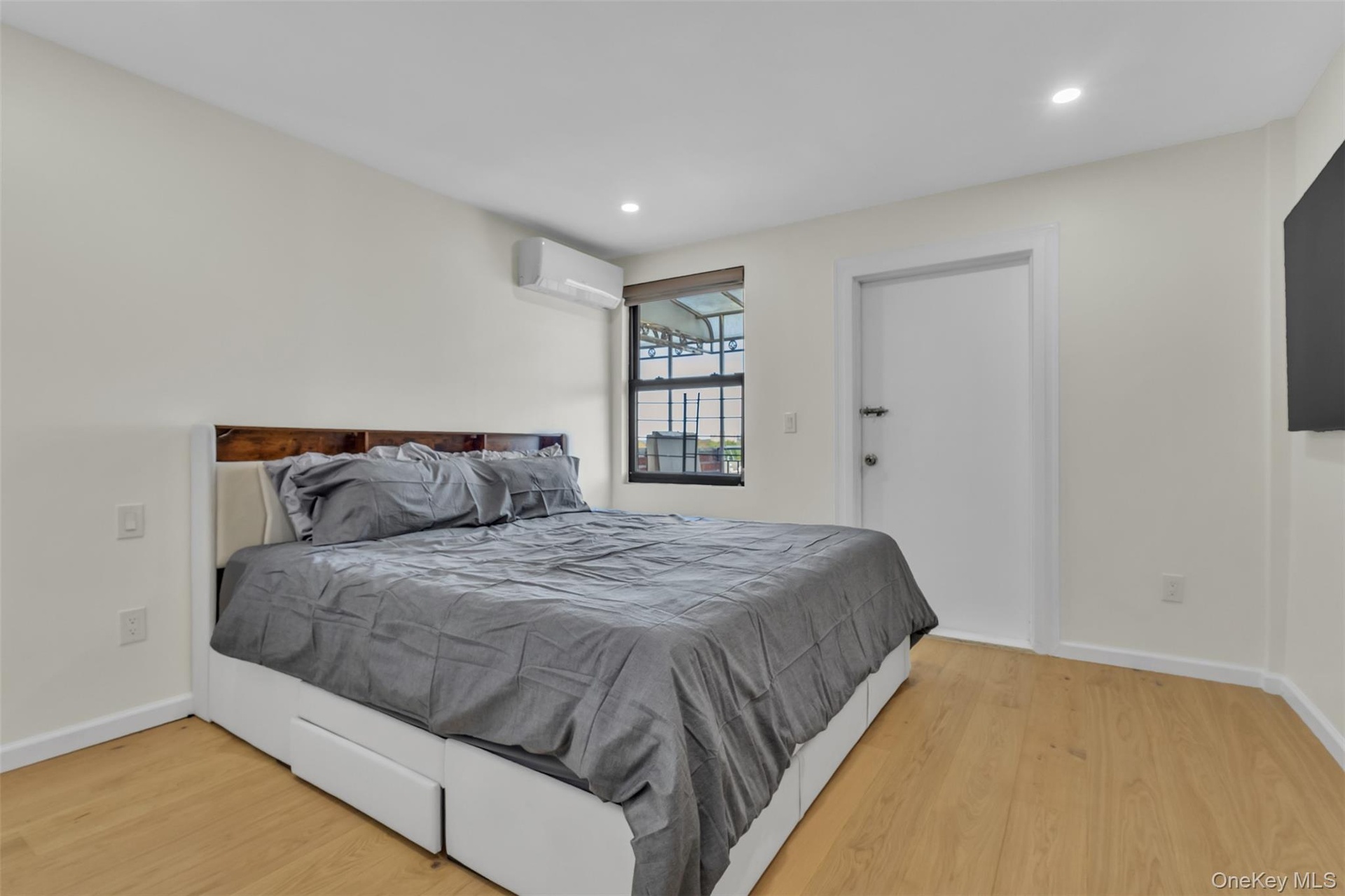Room featuring neutral wall paint, wood-finish flooring, recessed lighting, a window with integrated shade, and a wall-mounted ductless climate contro
