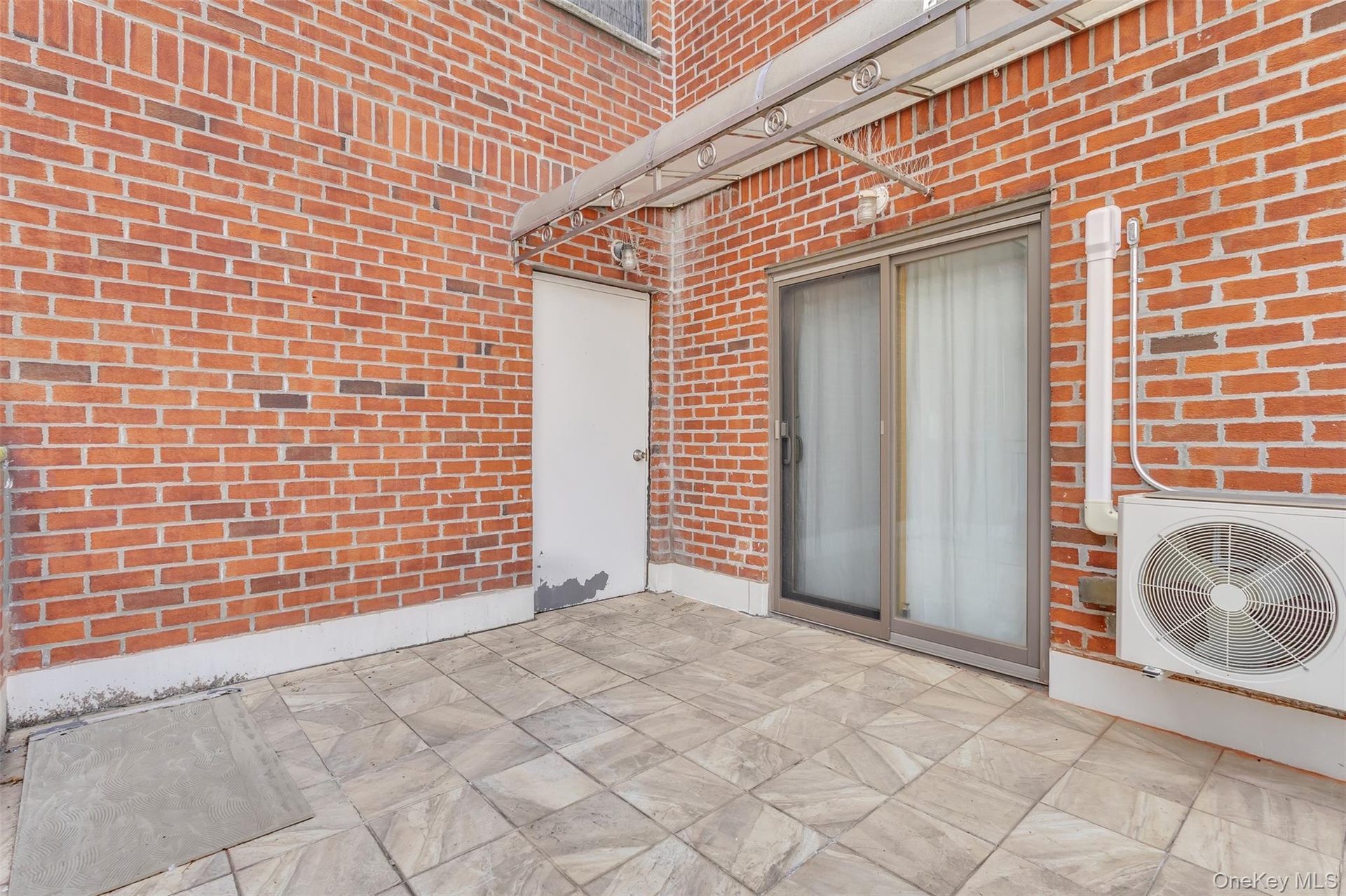 Outdoor terrace featuring red brick walls, tiled flooring, a sliding glass door, an attached metal awning, and wall-mounted exterior lighting