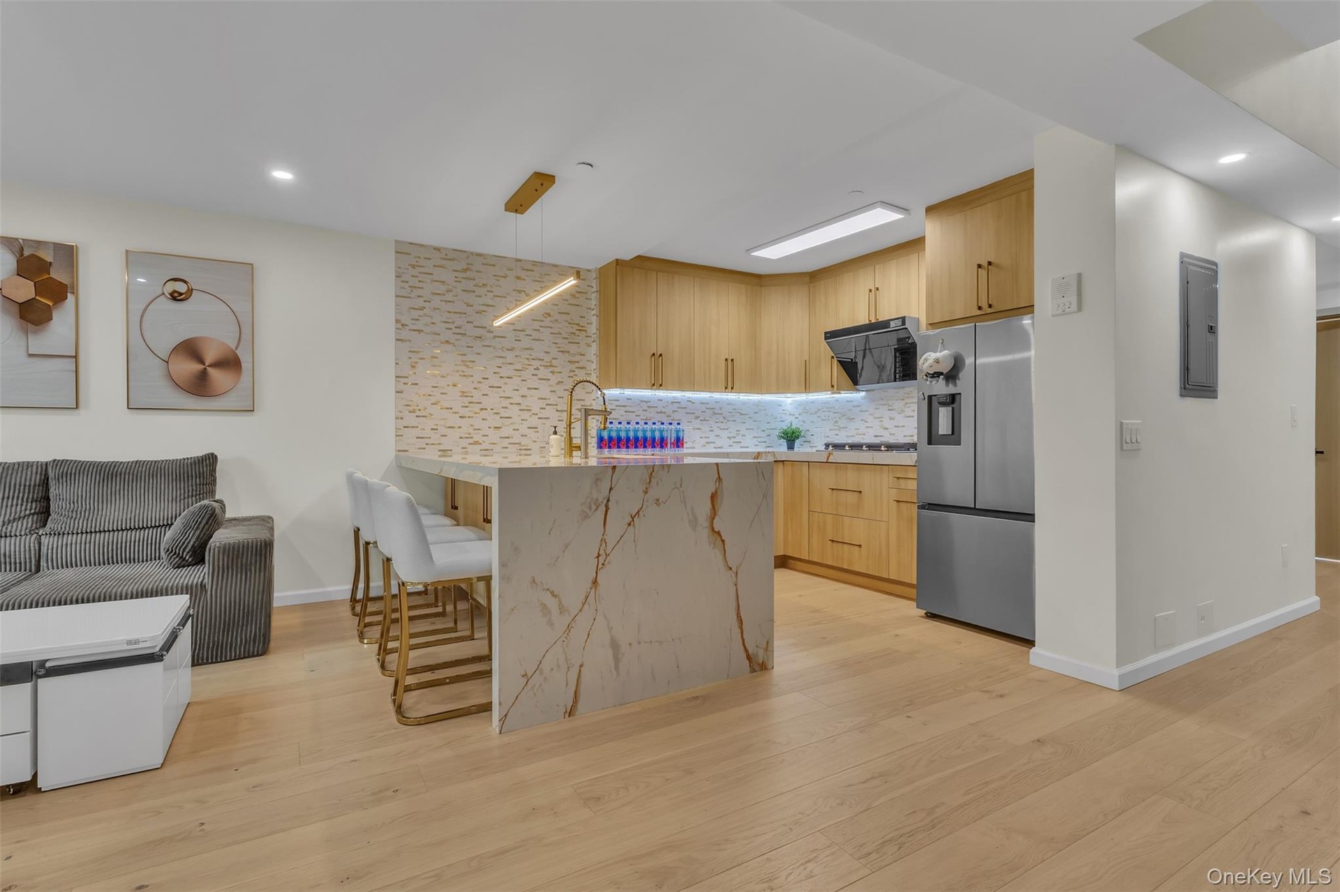 Kitchen featuring light wood-finish cabinetry, a waterfall-edge stone island, a decorative stone backsplash, recessed lighting, and stainless steel ap