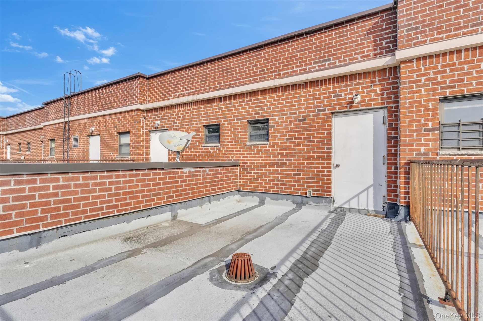 Flat rooftop terrace featuring a brick exterior wall, metal railing, and a drainage access point