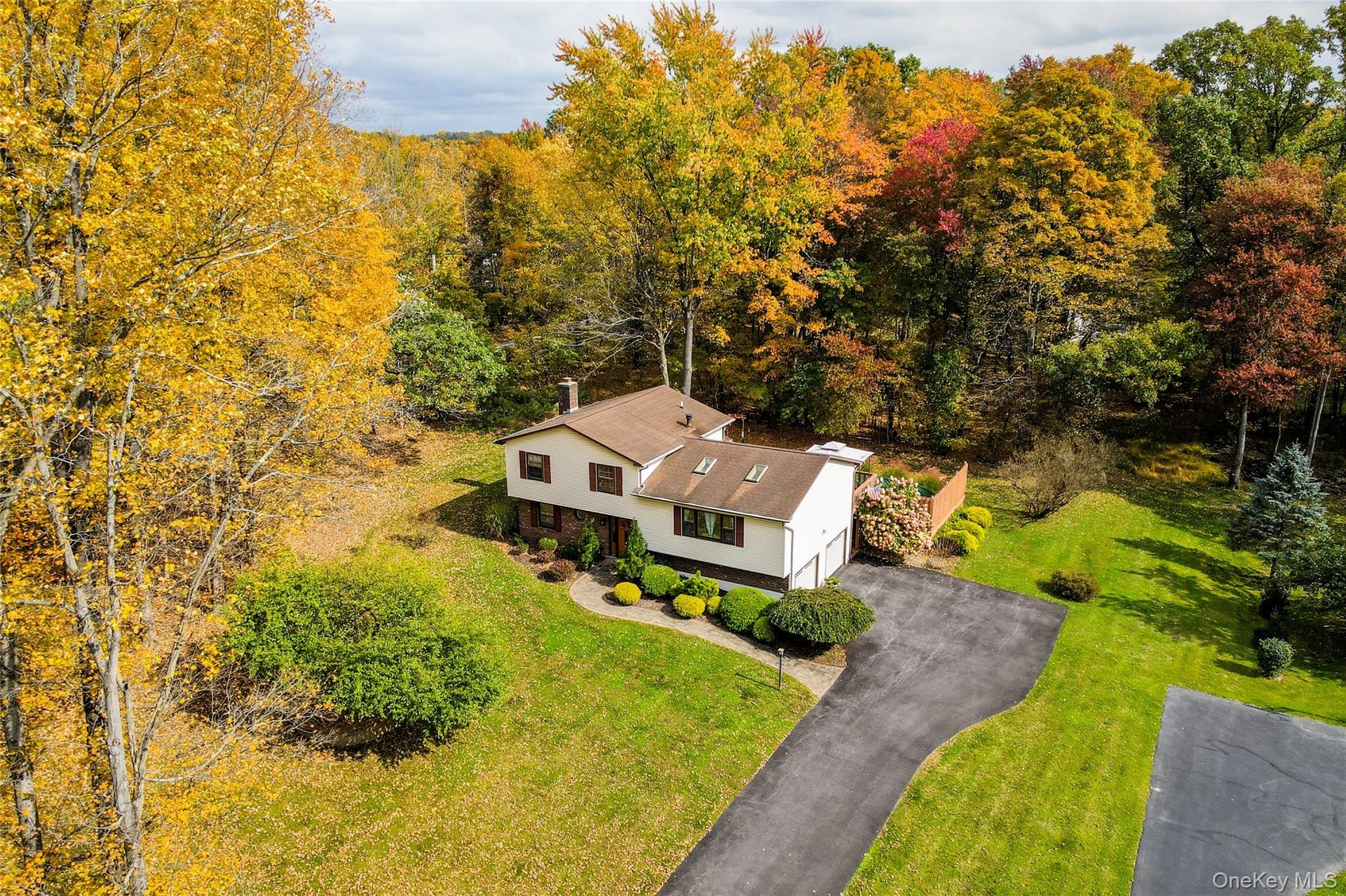 Split-level residence featuring a multi-tone exterior, asphalt driveway, two attached garage bays, roof-mounted skylights, and a wood privacy fence