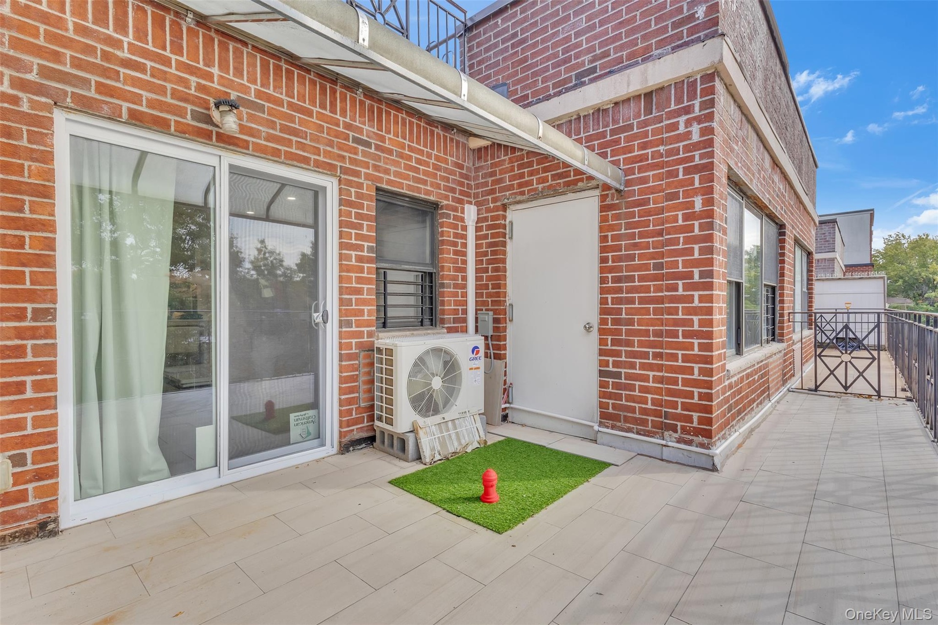 Exterior terrace featuring red brick masonry, tile flooring, a metal railing, and a sliding glass door