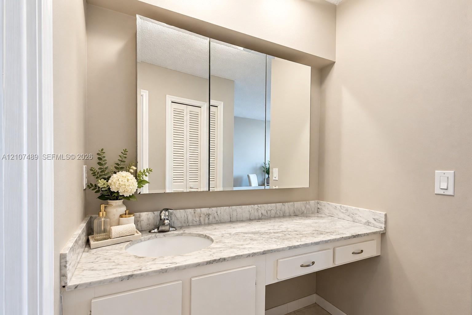 Vanity featuring a stone-patterned countertop, integrated basin with a chrome faucet, tri-fold mirrored medicine cabinet, and built-in drawers