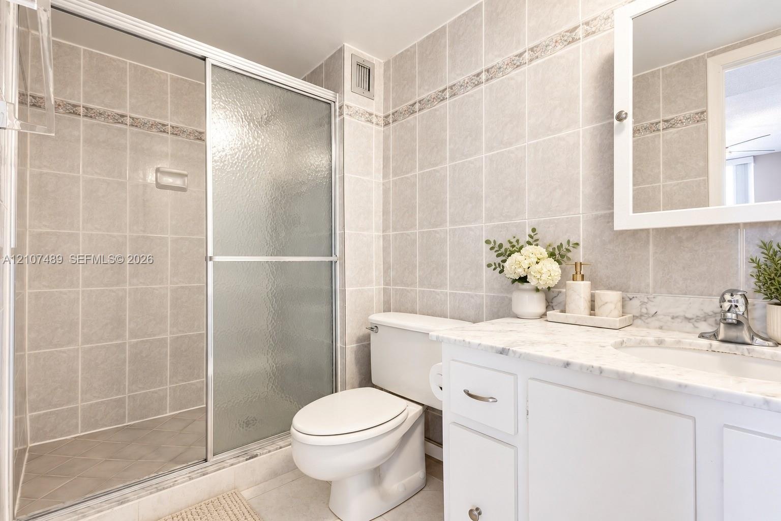 Bathroom featuring a shower with a sliding glass door, white vanity with stone-finish countertop, undermount sink, and tiled wall surround