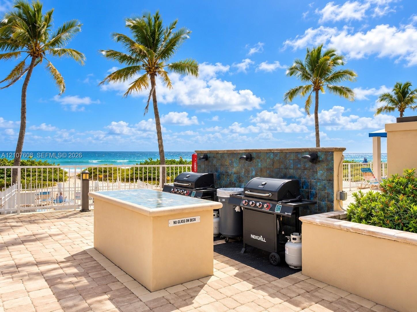 Outdoor patio featuring paver flooring, a stucco-finish built-in prep island with a stone surface, tiled backsplash, and metal perimeter fencing