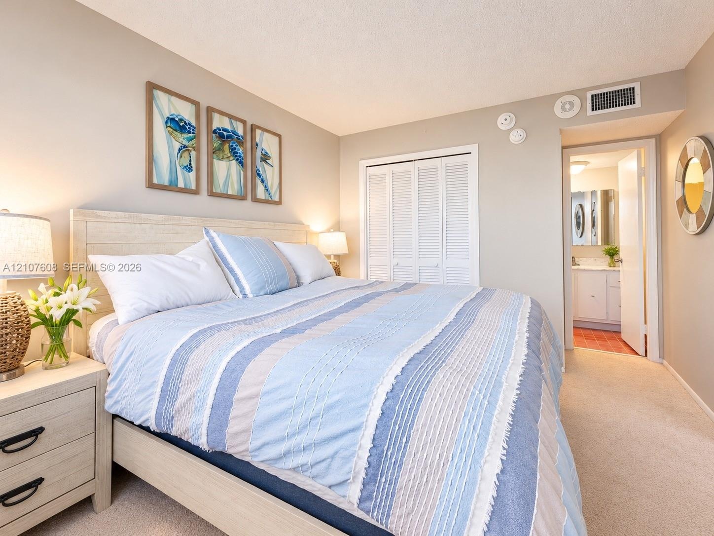 Neutral wall tones featuring carpeting, a double-door louvered closet, and an entry to an en-suite bathroom with a vanity