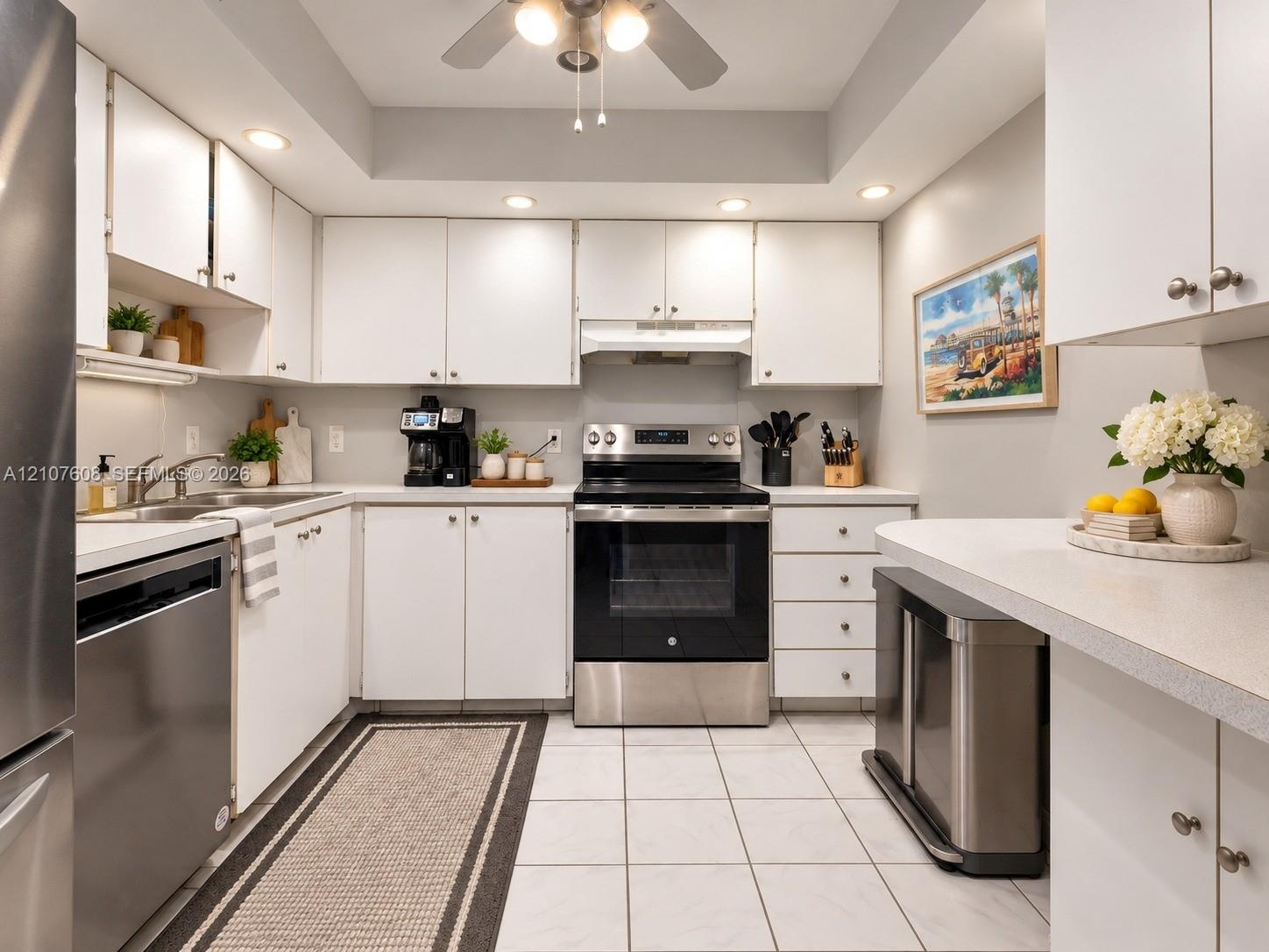 Kitchen featuring white shaker-style cabinetry, stainless steel appliances, recessed ceiling lighting, light-toned tiled flooring, and a peninsula cou