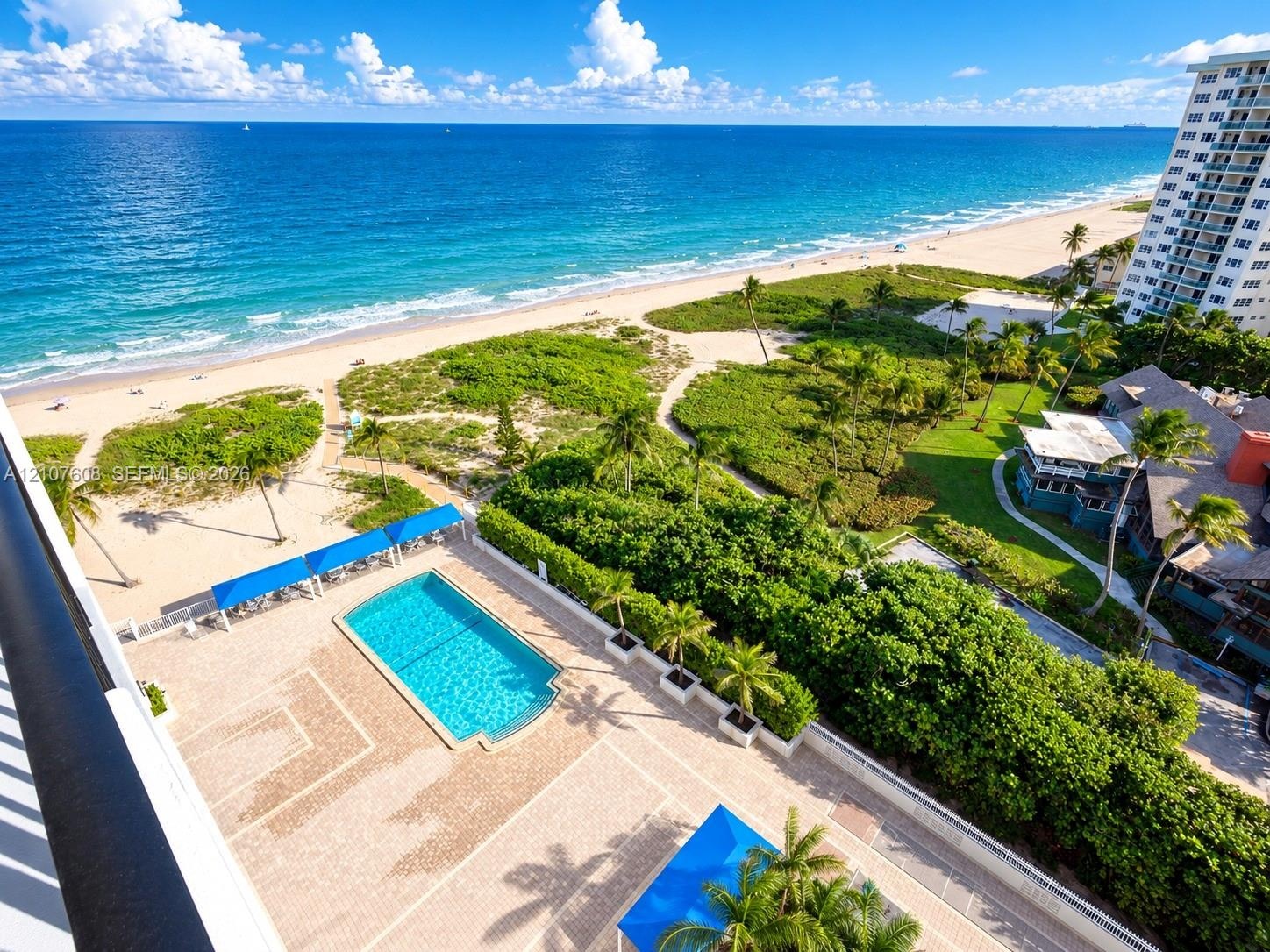 Oceanfront balcony featuring a rectangular swimming pool, paver deck, permanent shade structures, and manicured landscaping