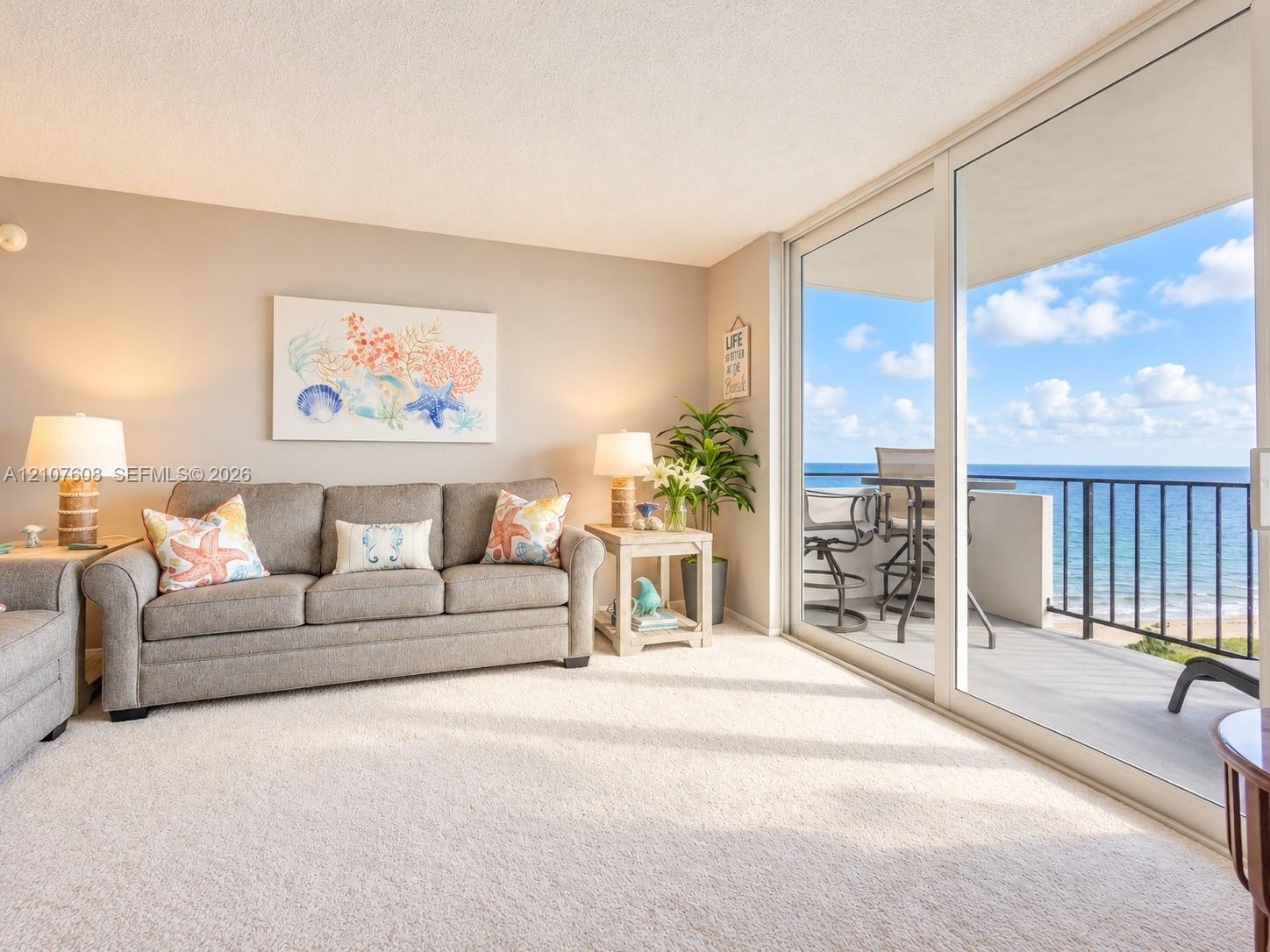 Living area featuring wall-to-wall carpeting and floor-to-ceiling sliding glass doors opening to a balcony with metal railings and coastal surrounding