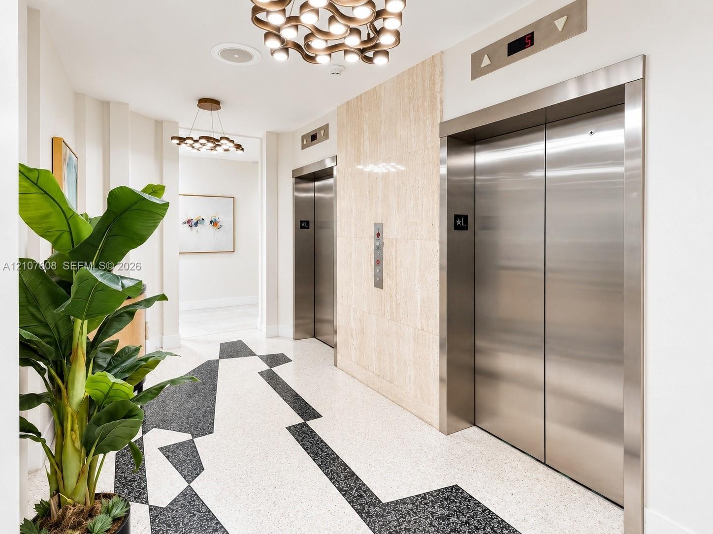 Elevator lobby featuring stainless steel doors, stone-tiled accent wall, geometric terrazzo flooring, and modern multi-bulb chandeliers