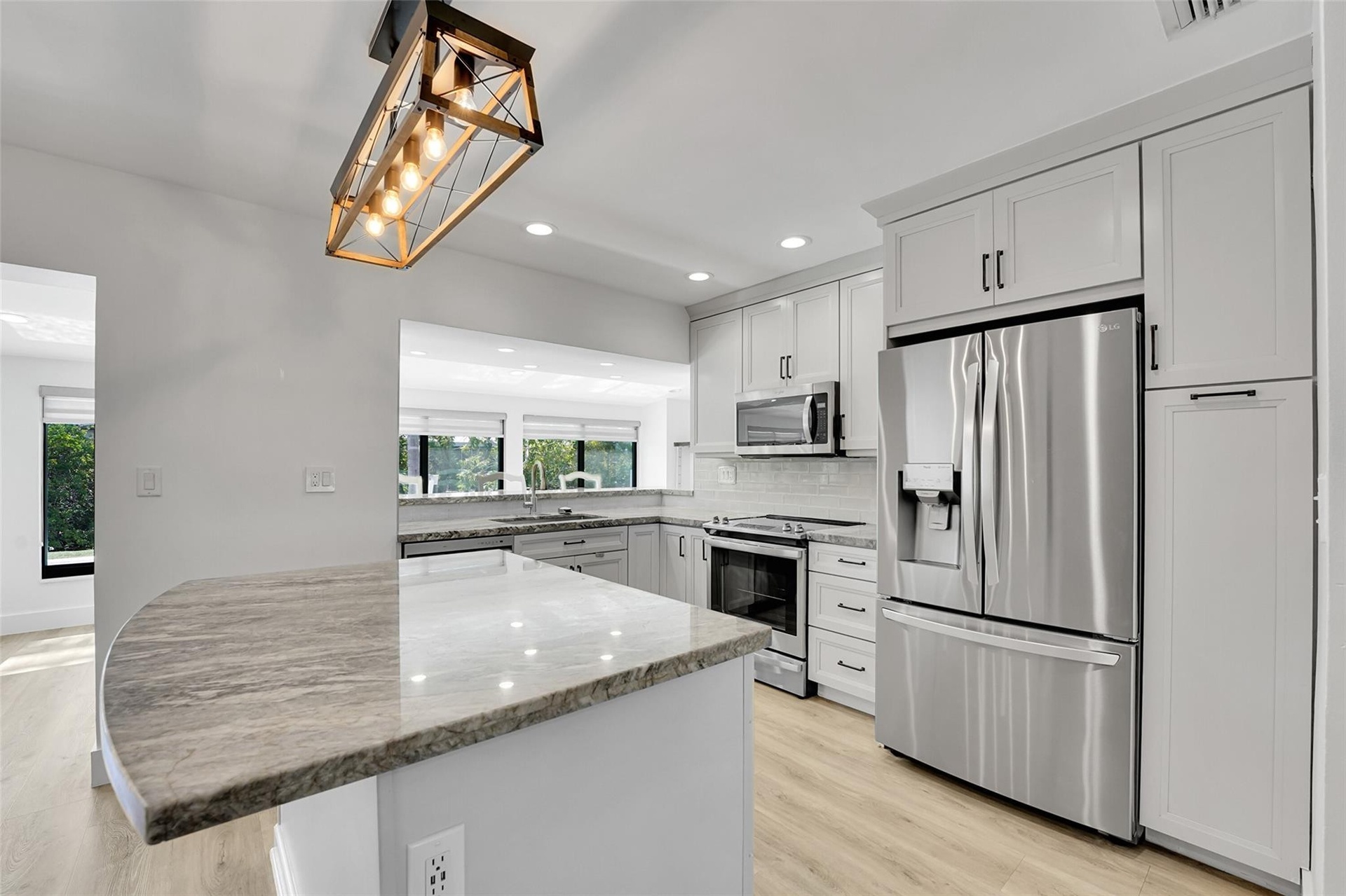 Kitchen featuring a curved peninsula island with a polished countertop, stainless steel appliances, light wood-finish flooring, white shaker-style cab