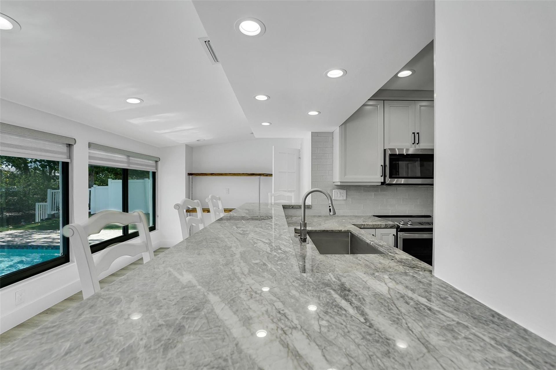 Kitchen featuring a large light-toned countertop, stainless steel sink with a gooseneck faucet, white cabinetry, and stainless steel microwave
